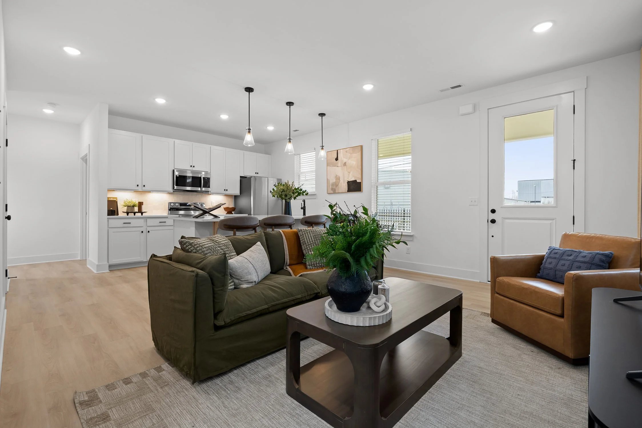 Open-concept living room and kitchen with white cabinets, bar stools, and contemporary decor.