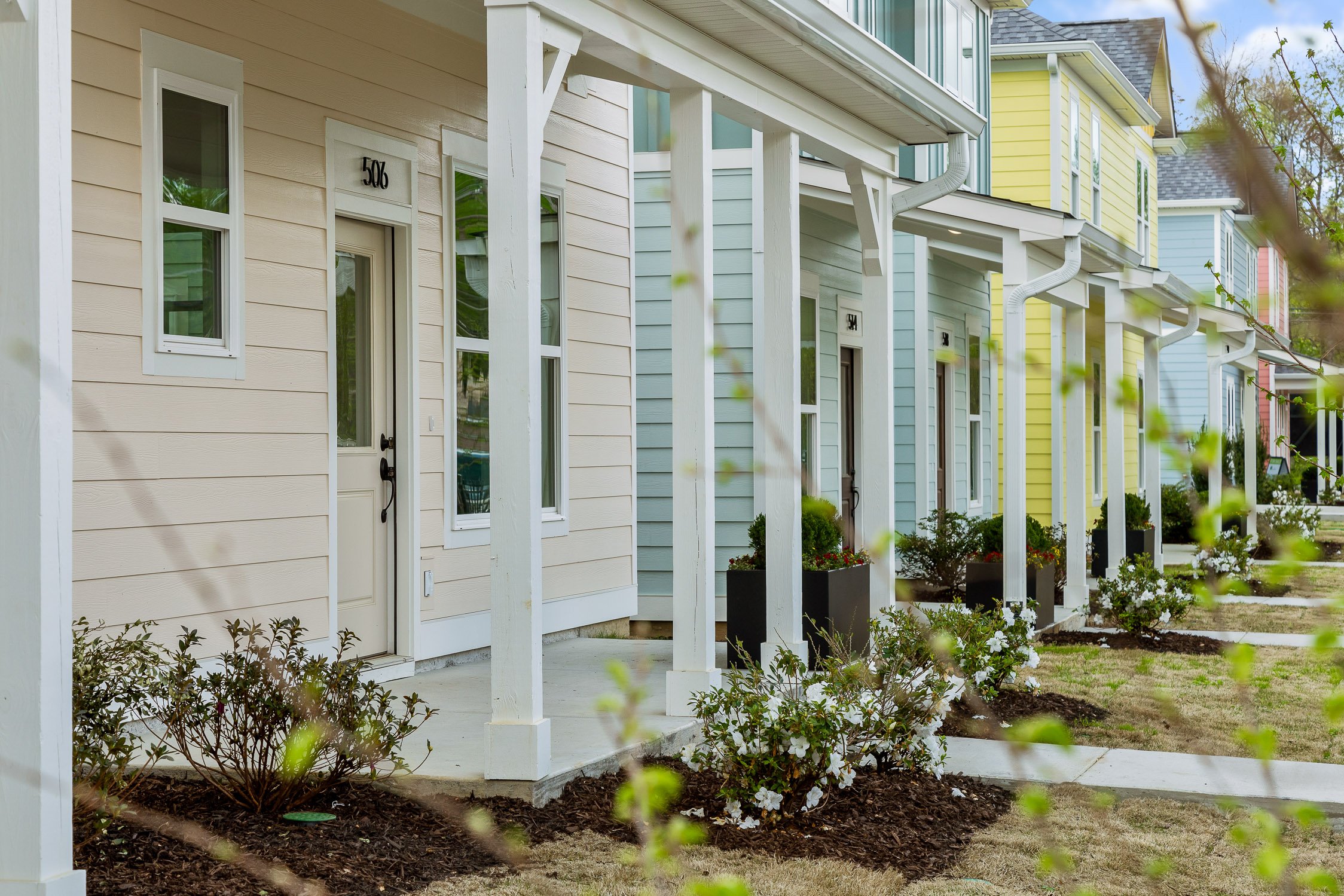 Colorful row of modern townhouses with front porches, planters, and plants in a residential neighborhood.