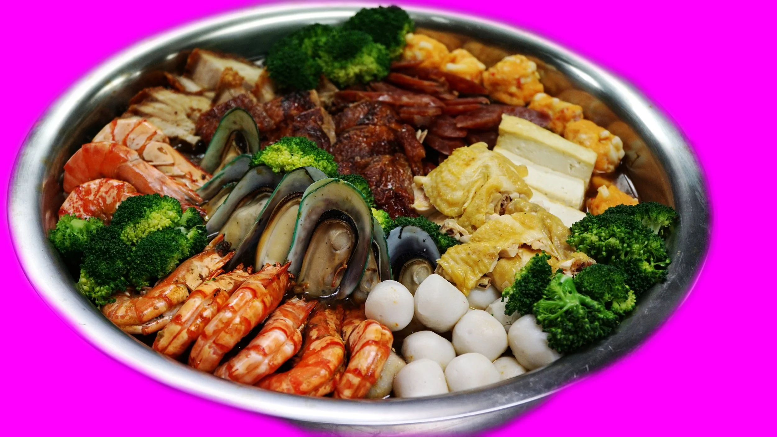 Een grote metalen schaal "Poon Choi" gevuld met een assortiment van zeevruchten, groenten, vlees en kaas, inclusief garnalen, mosselen, broccoli, quiches, vleeswaren, en soja kip, op een roze achtergrond.