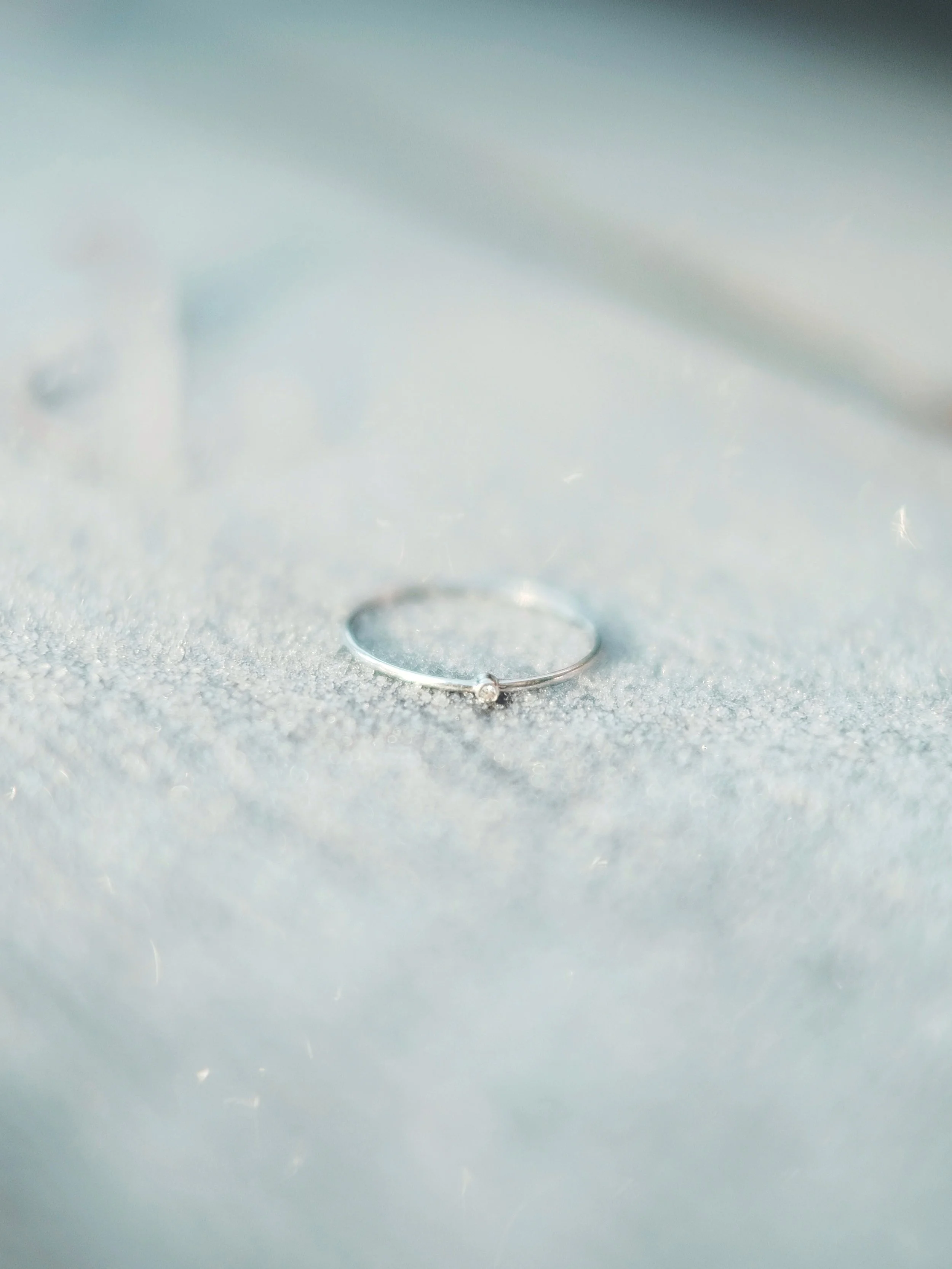 A close-up of a dainty and equisite 925 Sterling silver ring with a small gemstone, a natural diamond, resting on a soft, textured surface.