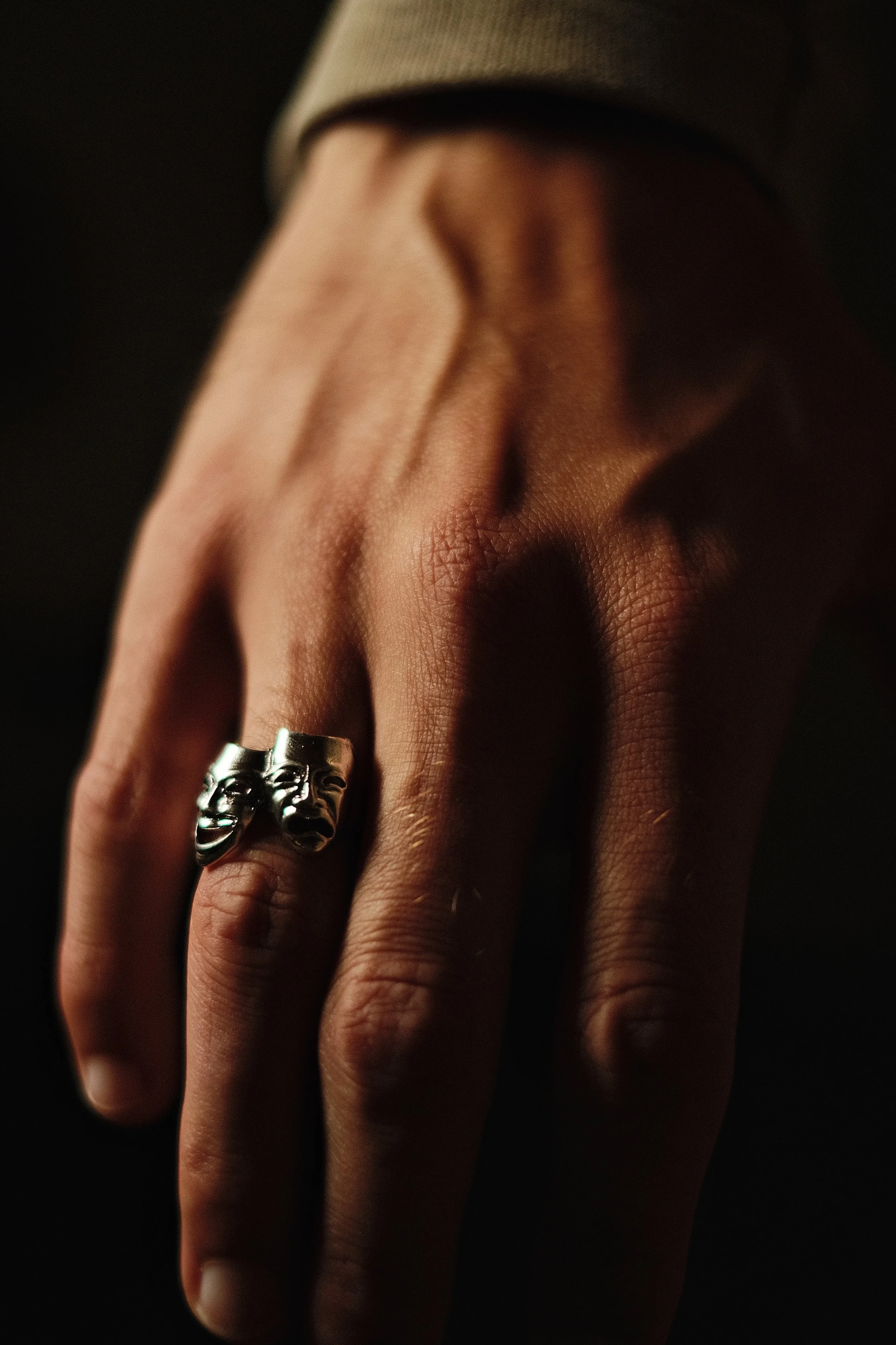 Close-up of a hand wearing a silver ring with two theatrical masks, one smiling and one frowning.