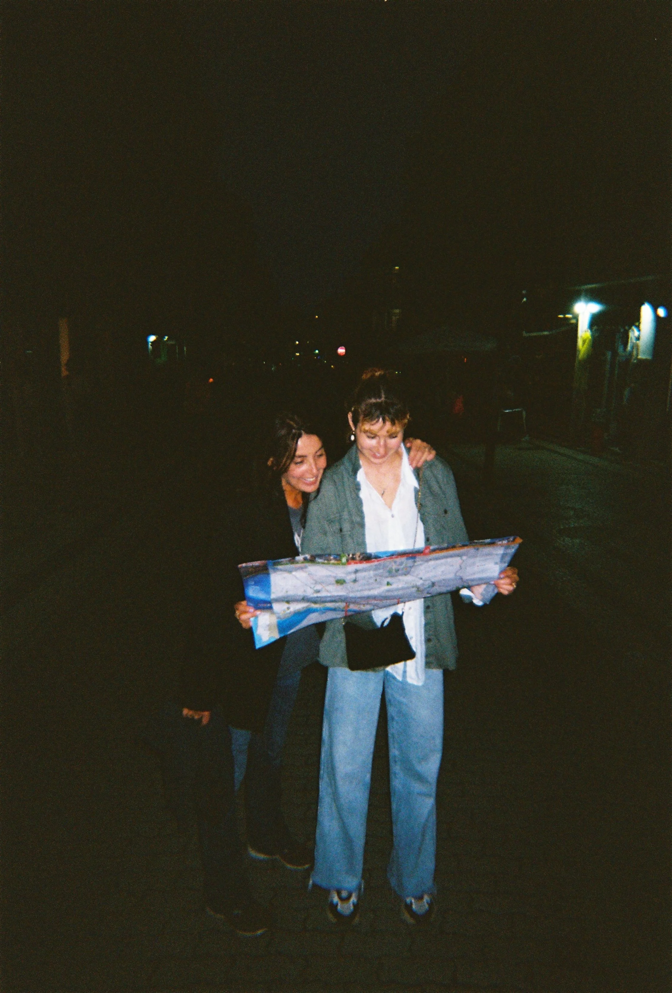 Two women from Lucchini Moon standing outdoors at night, looking at a map together trying to find the artisan factories and best jewelry factiry to craft their own designs.