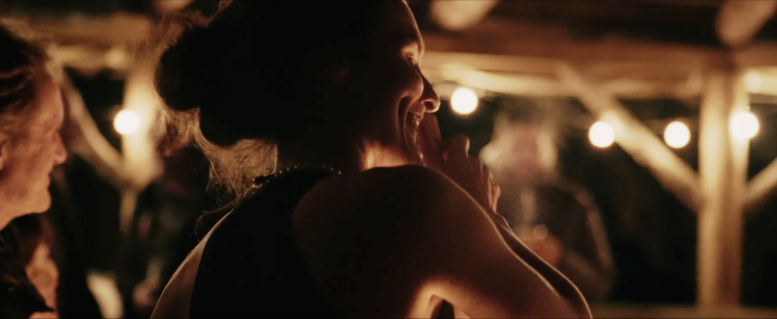 People laughing and enjoying themselves at an outdoor gathering at night, illuminated by string lights.