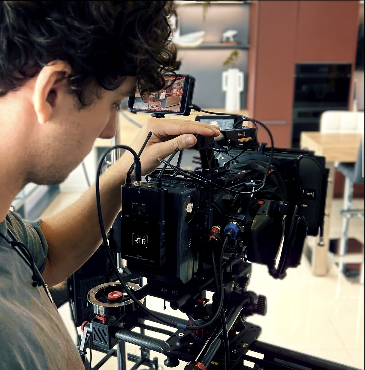 A man operating a professional video camera with mounted monitor in a modern indoor setting.