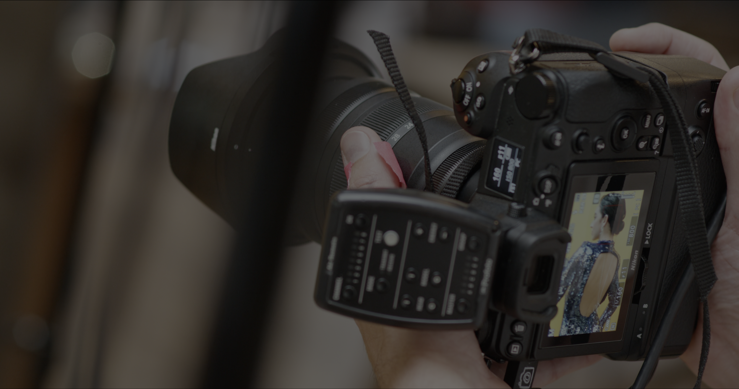 Close-up of a person holding a Nikon digital camera, capturing a photo of a woman with her hair in a bun wearing a traditional Japanese kimono with a floral pattern.