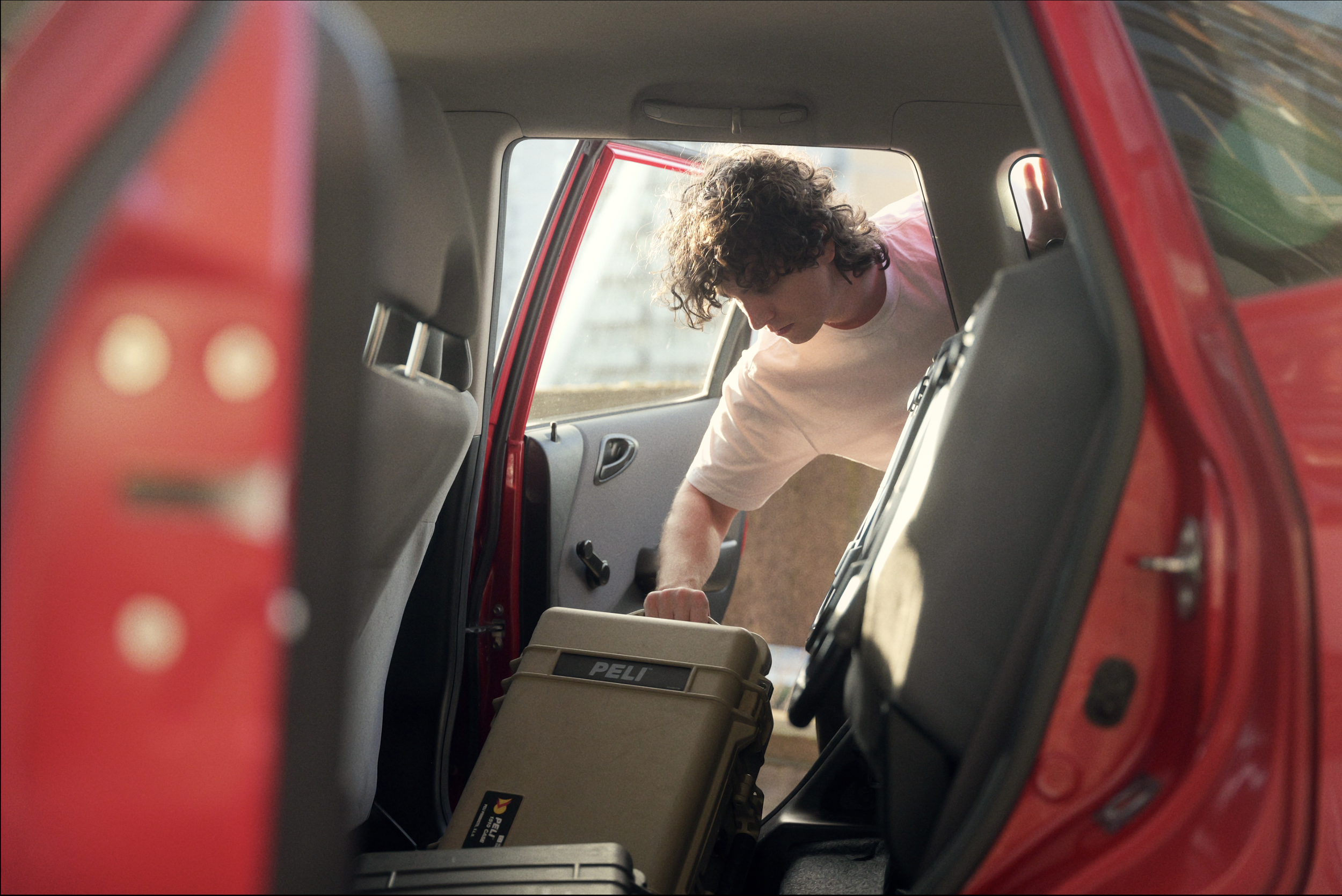 Luke McCulloch holding a camera case next to a red car