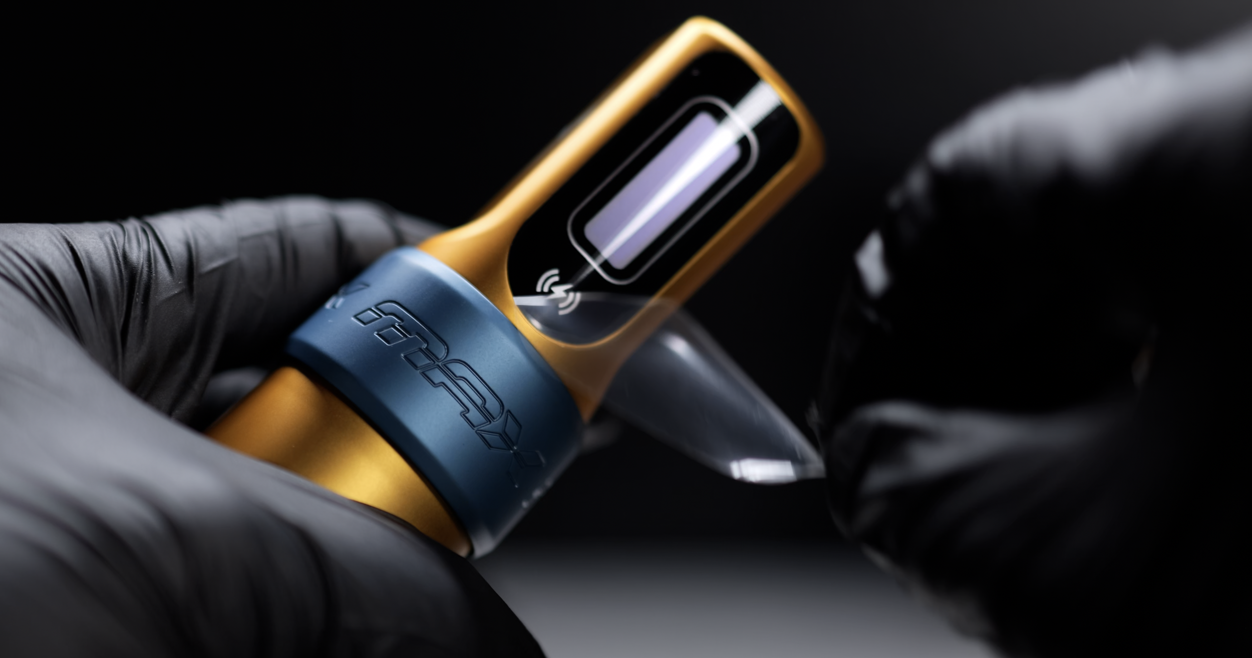 A person wearing black gloves holding a gold and blue vape with a digital screen displaying a charging indicator.