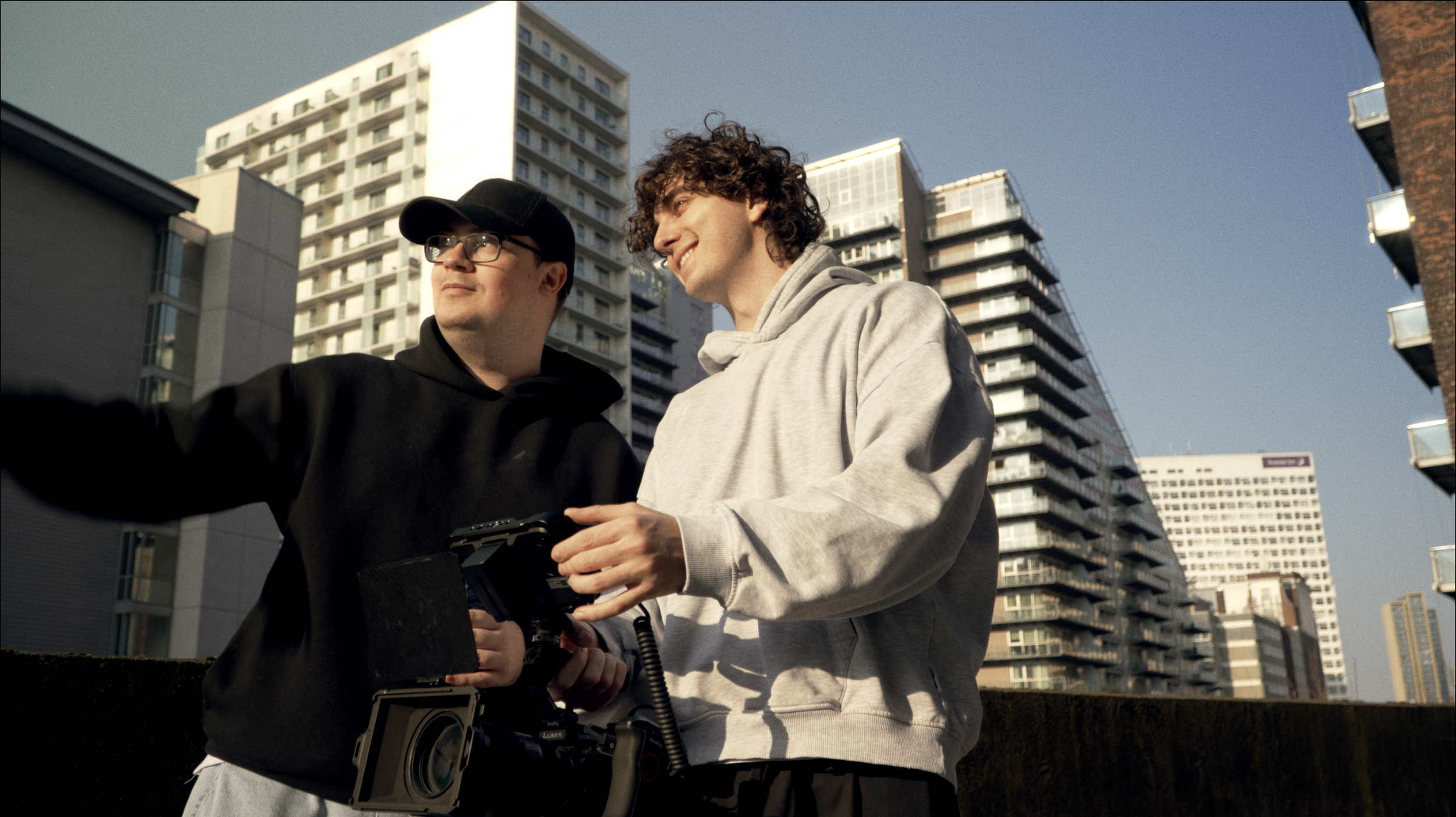 Luke McCulloch and his friend, Aviv, holding a camera with buildings in Manchester behind him.