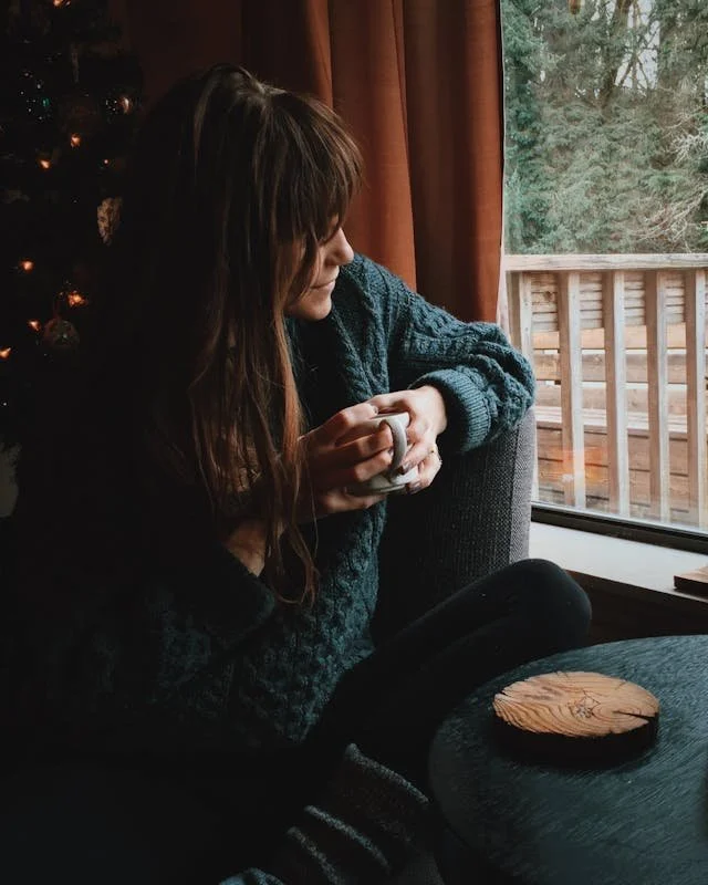 Serene moment of a woman enjoying a warm drink indoors by the window in a winter setting