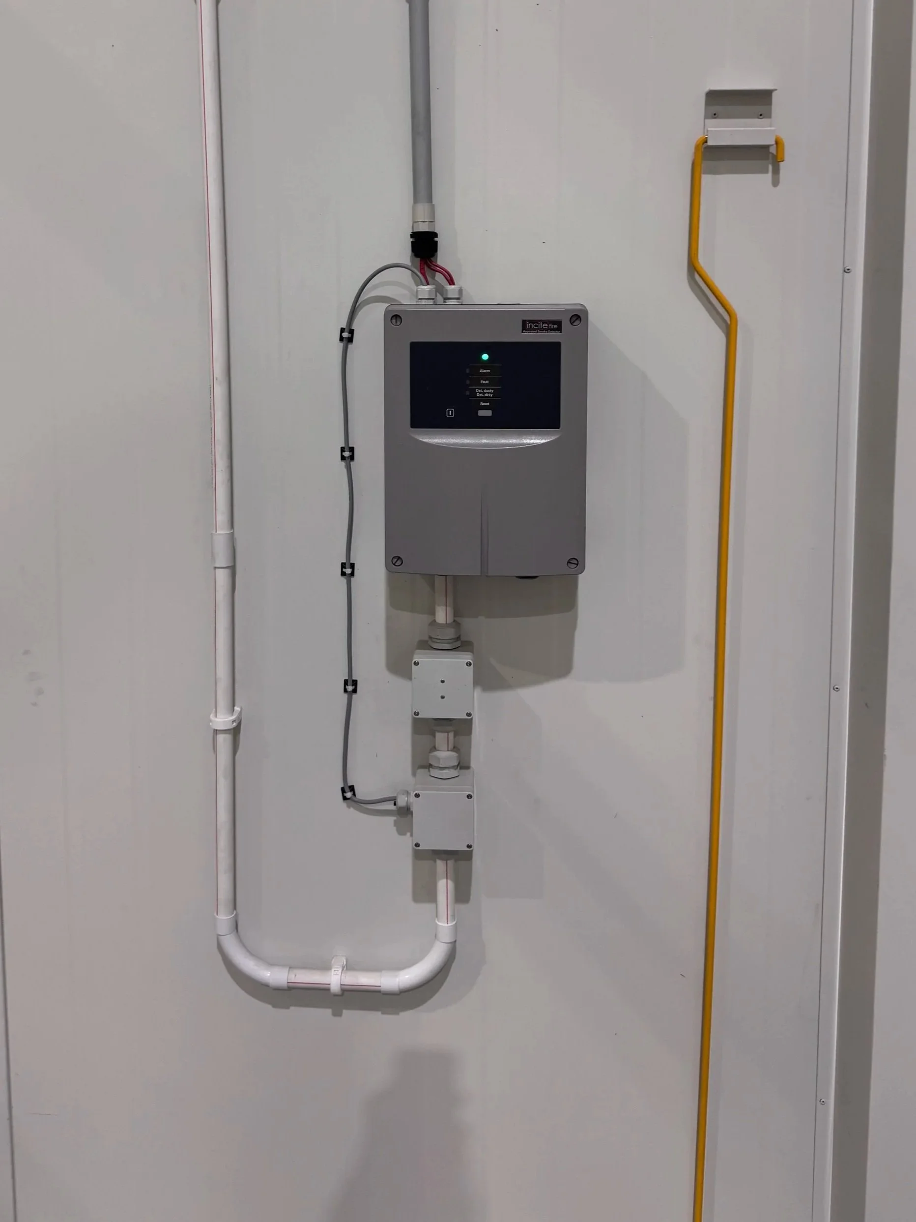 Electrical panel with white pipes, cables, and switches mounted on a white wall.