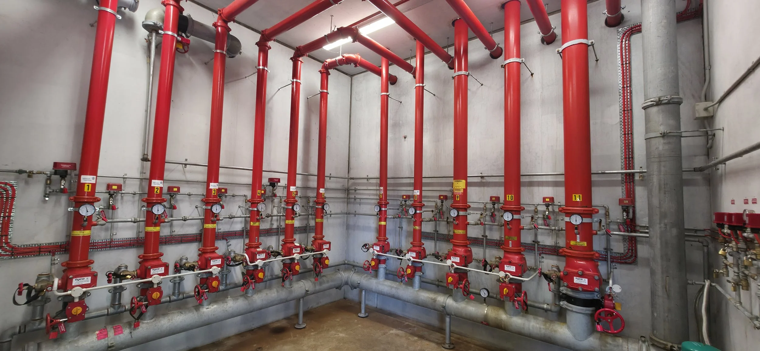 A mechanical room with multiple red pipes, gauges, and valves, each labeled with numbers from 1 to 11, connected to a building's plumbing or fire sprinkler system.