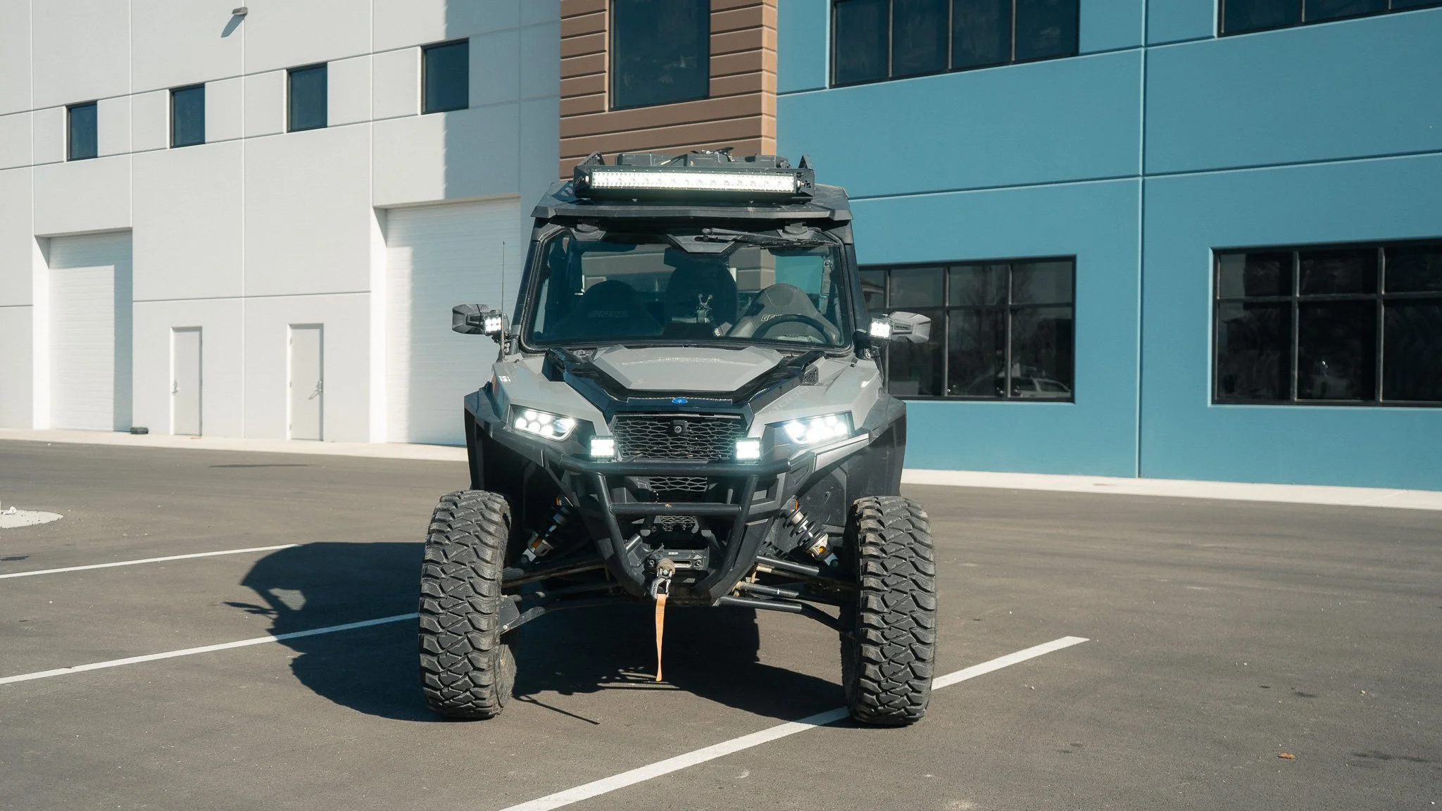 A black off-road utility vehicle parked in an empty parking lot in front of a modern building with white, blue, and brown walls.