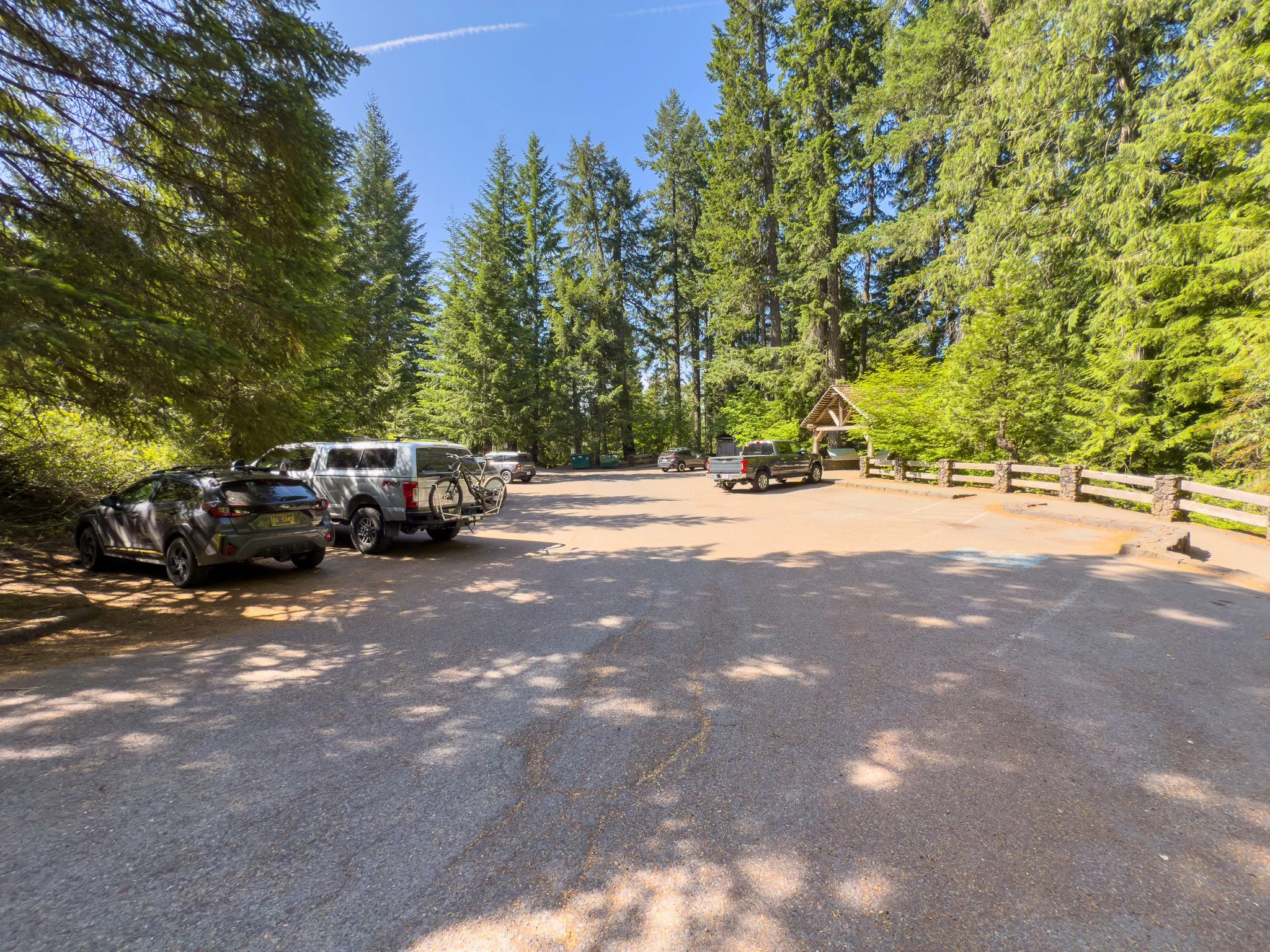 Spacious parking area at the Sahalie Falls trailhead, surrounded by tall evergreens under a clear blue sky.