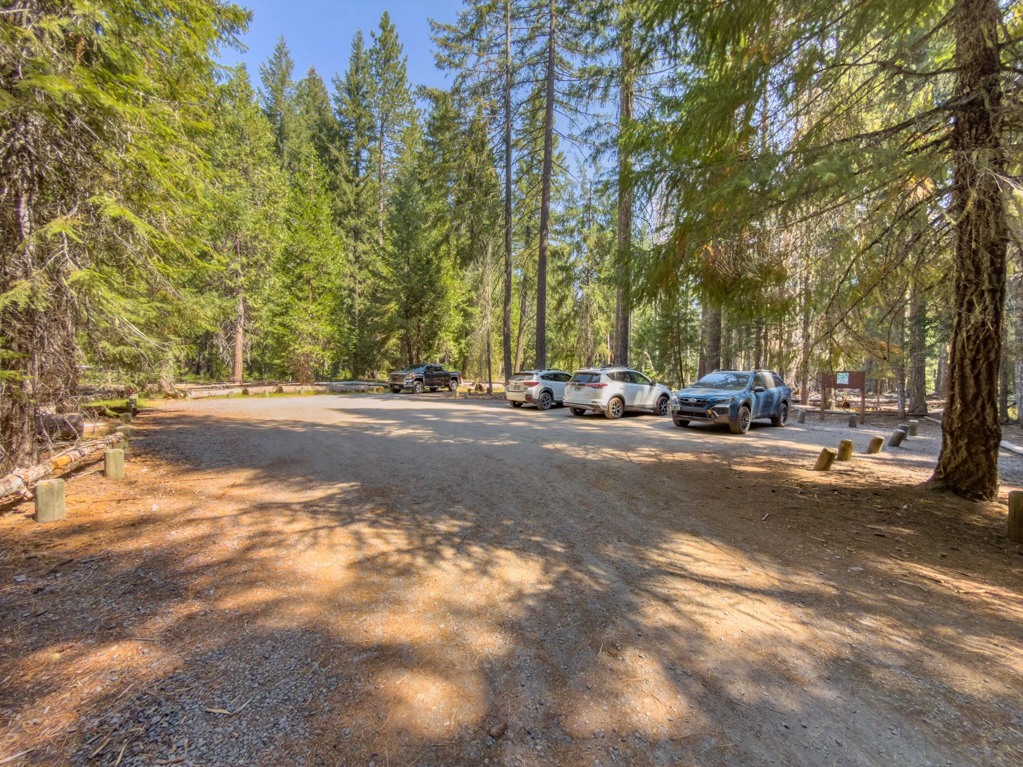 Gravel parking area at the National Creek Falls trailhead, surrounded by tall conifers on a sunny day