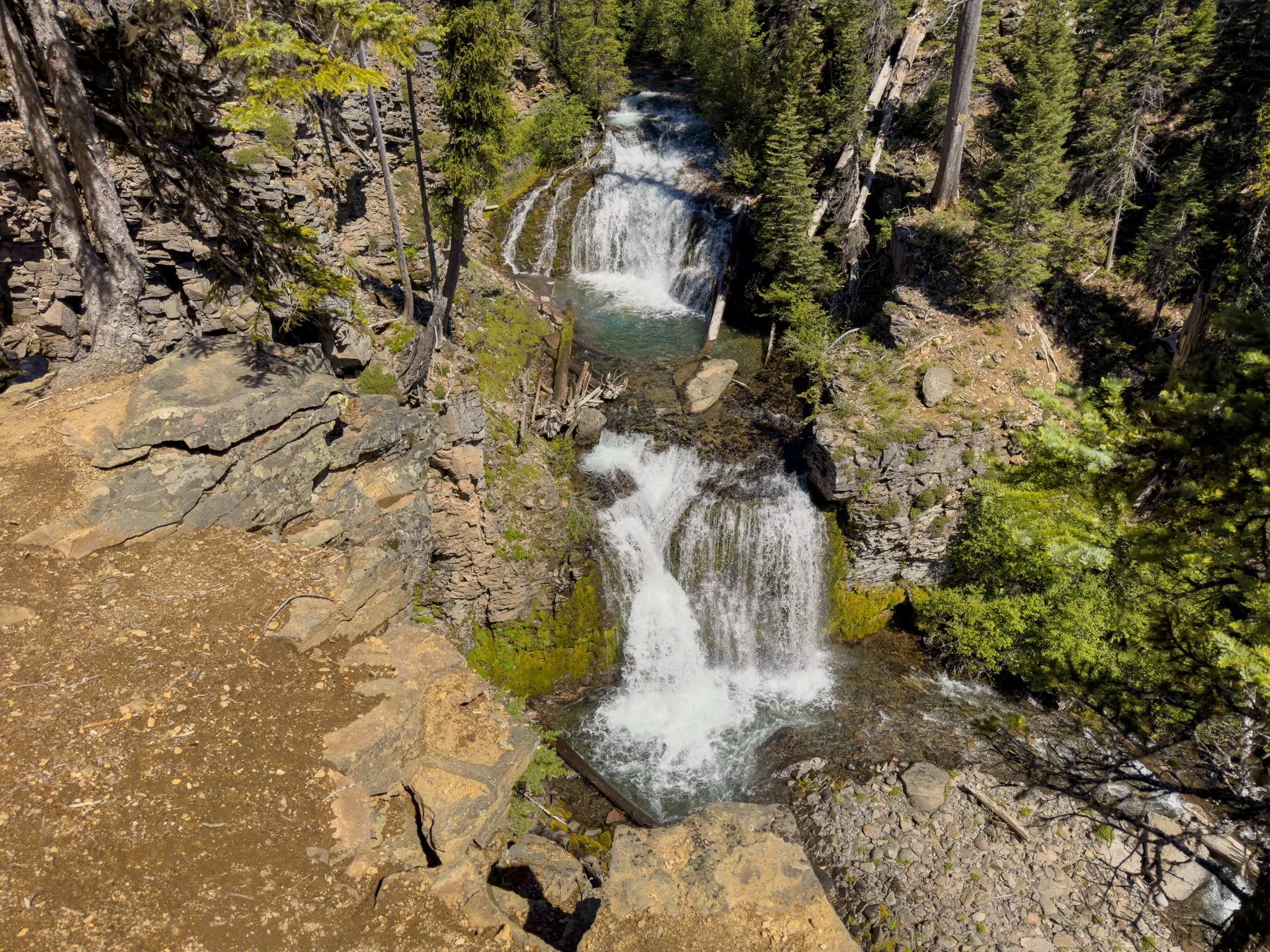 Double Falls cascading over two basalt ledges into emerald pools below, viewed from the cliffside overlook along the Tumalo Falls Trail in Deschutes National Forest.
