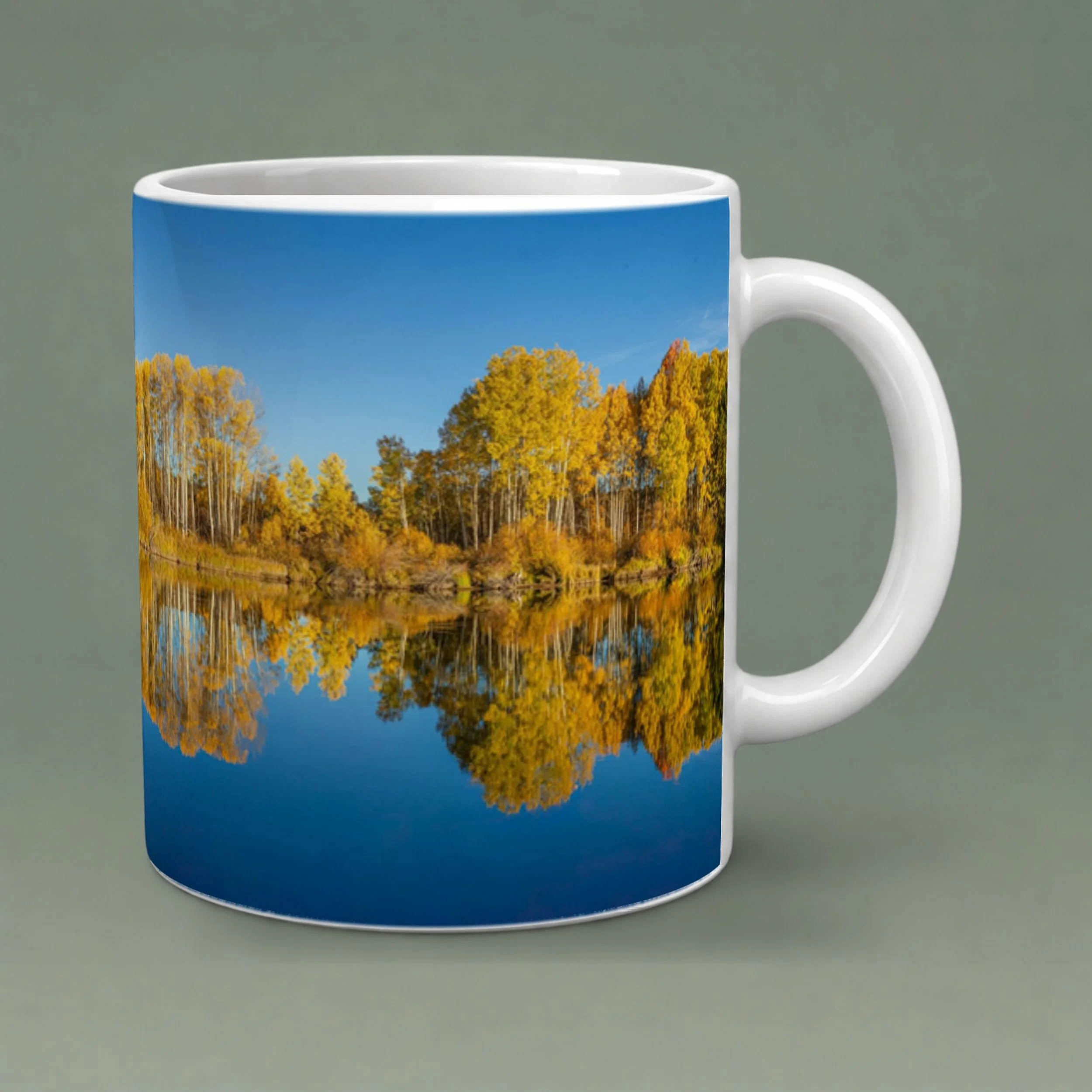White 11 oz ceramic mug featuring golden autumn trees reflected in Oregon’s Deschutes River, with a rounded handle and gray-green background.