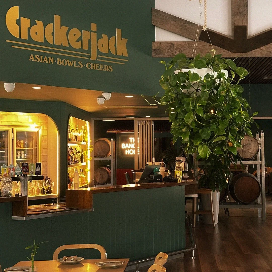 Inside a restaurant with a green and wood decor, a bar area with bottles, and a large potted plant hanging from the ceiling.