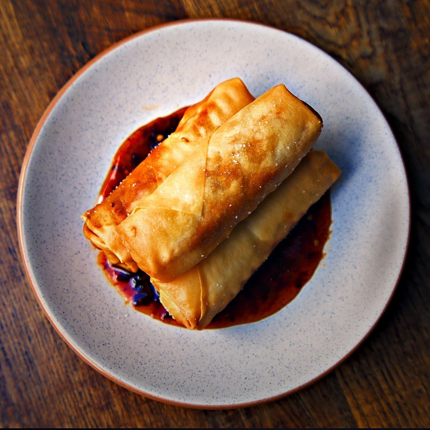 Two spring rolls on a white plate with a red sauce, placed on a wooden table.