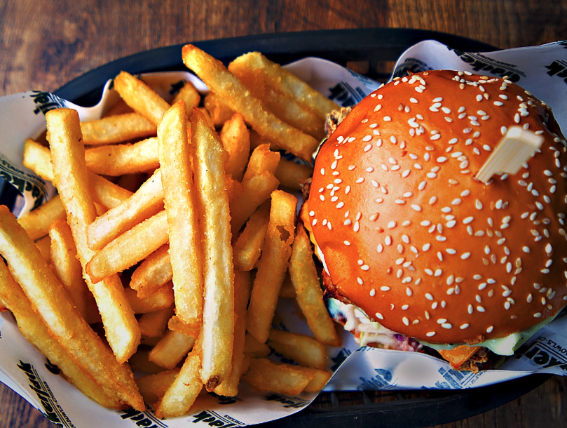 French fries and a cheeseburger with sesame seed bun on a black tray.
