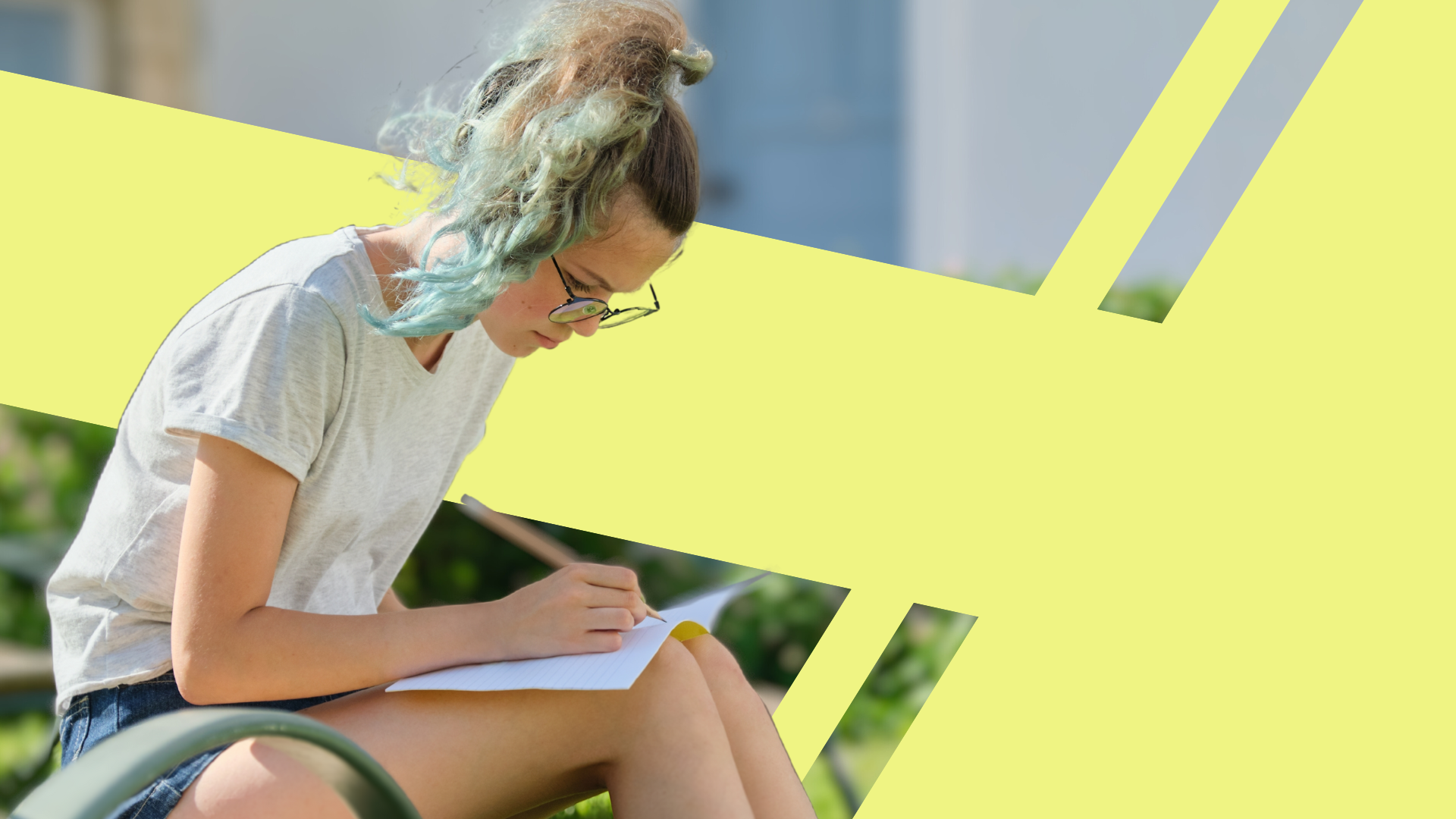 A young woman with colorful hair, glasses, and a white t-shirt sitting outdoors, writing in a notebook.