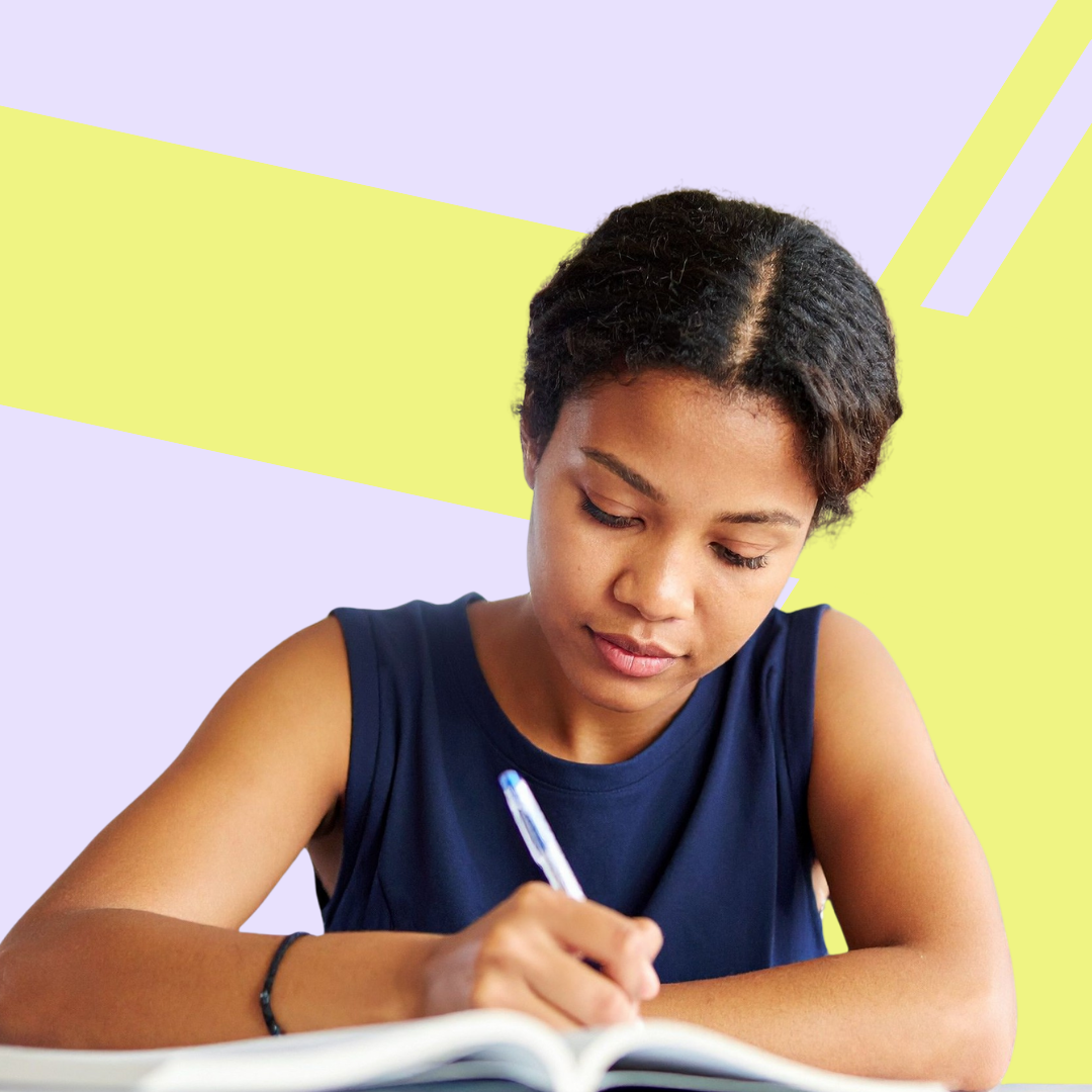 A young woman with short curly hair is sitting at a desk, writing in a notebook with a pen, against a pastel-colored background.