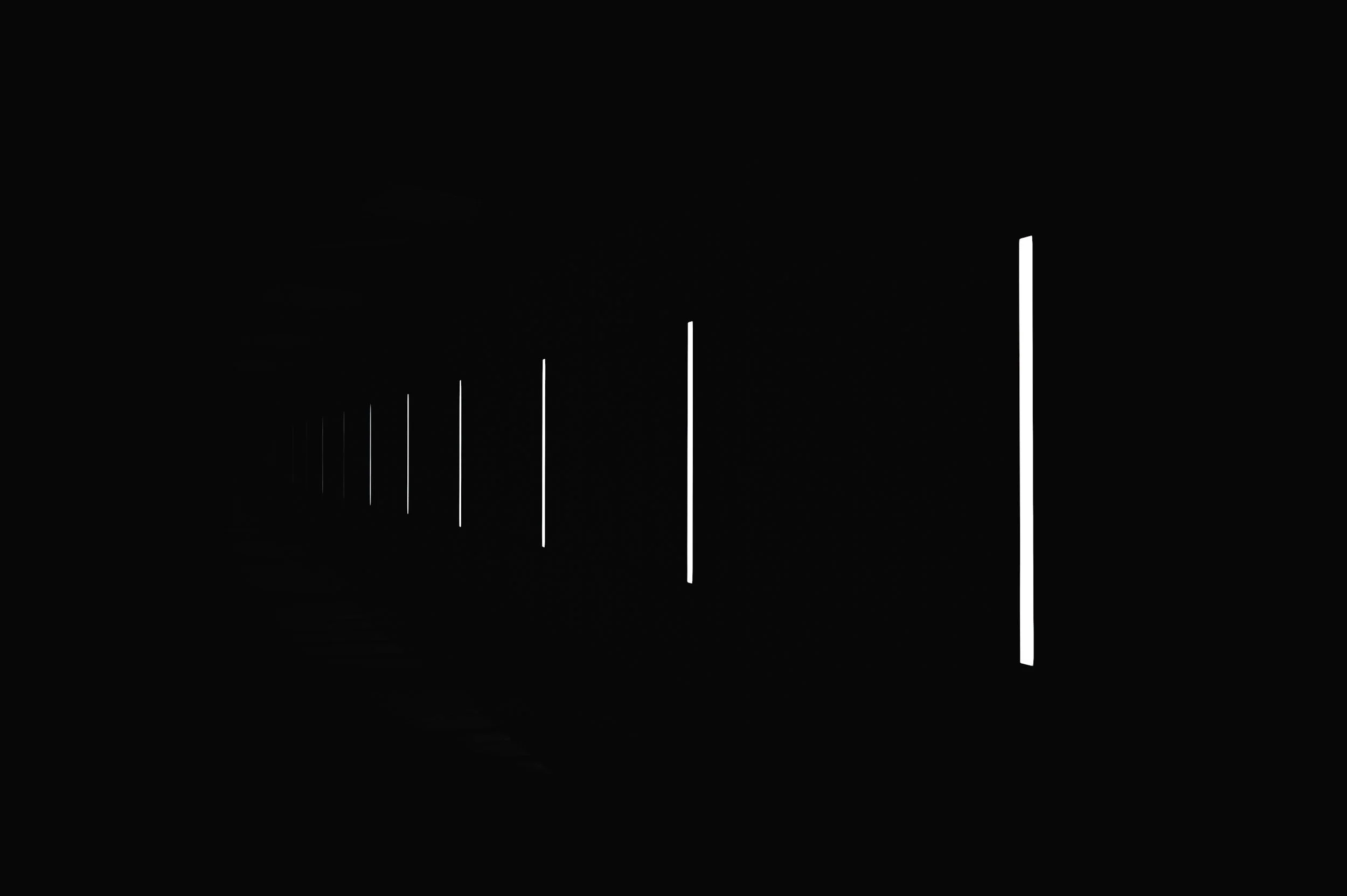 A series of vertical white lights decreasing in size and spacing from right to left inside a dark room, creating a perspective illusion.