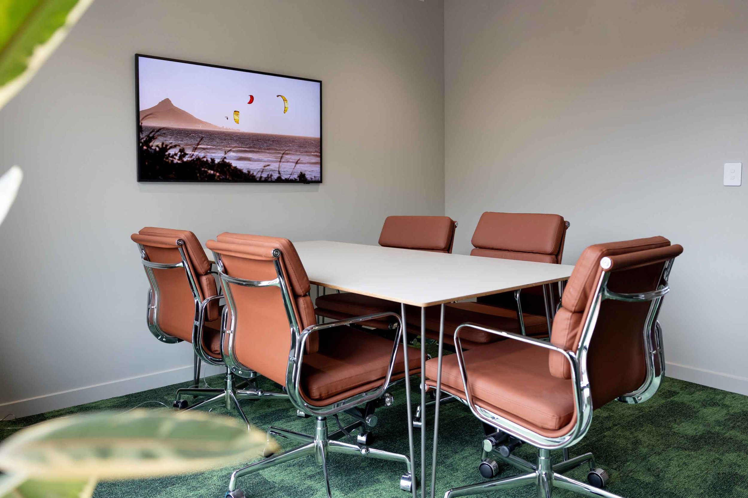Modern meeting room with brown chairs, white rectangular table, and a wall-mounted landscape artwork.