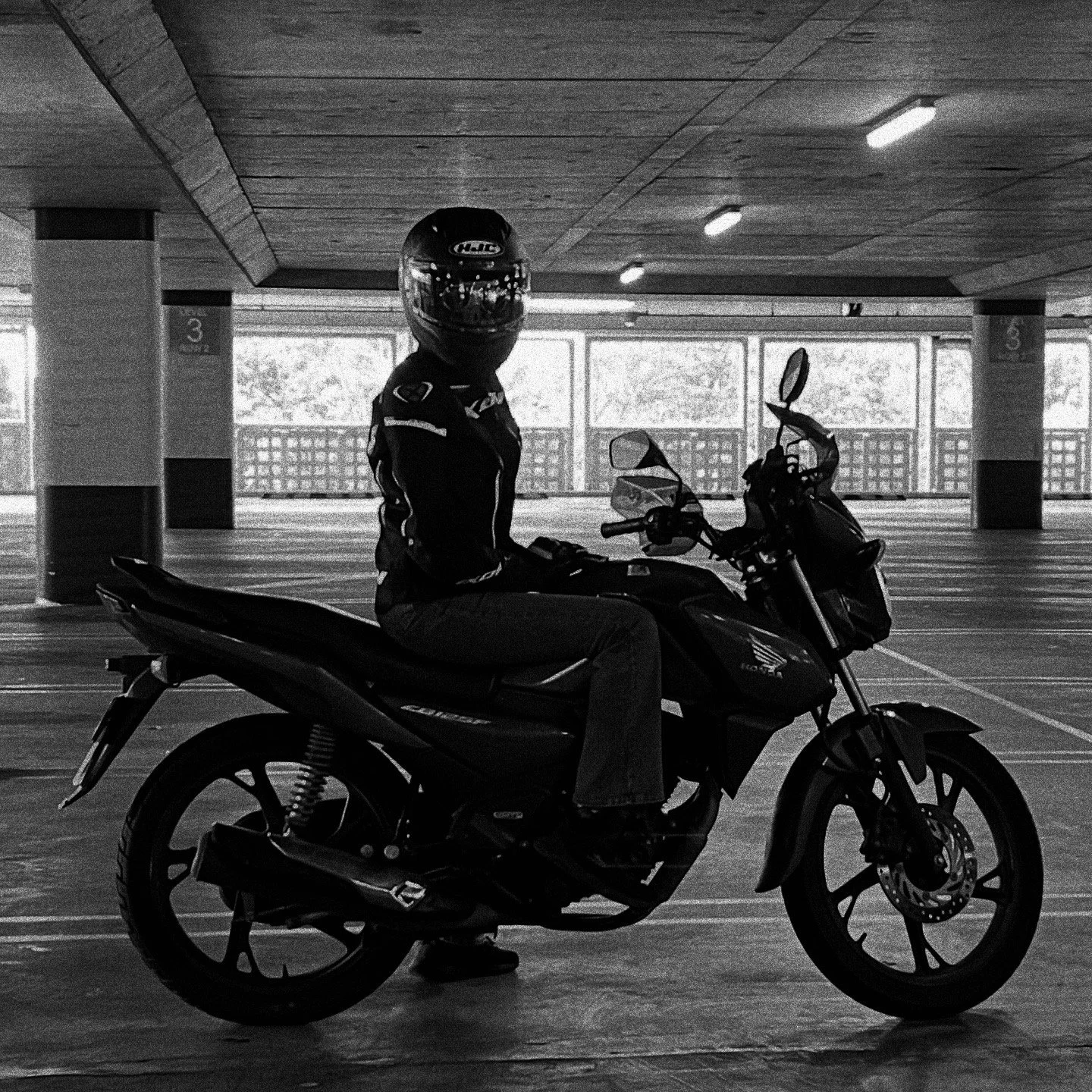 A person wearing a helmet and motorcycle gear sitting on a black Honda motorcycle in an empty indoor parking garage.