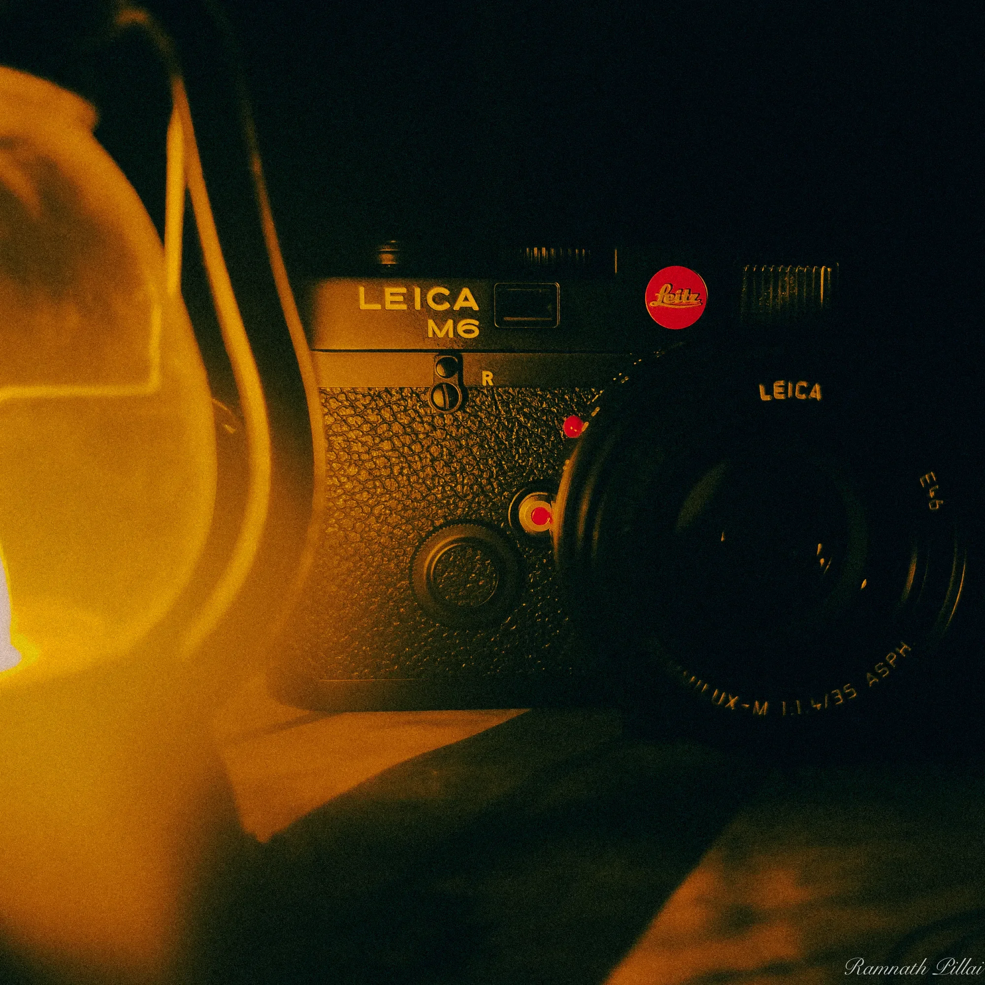 Close-up of a Leica M6 camera with a Leica lens, illuminated by warm light, seen from above, with parts of a yellow object on the left.