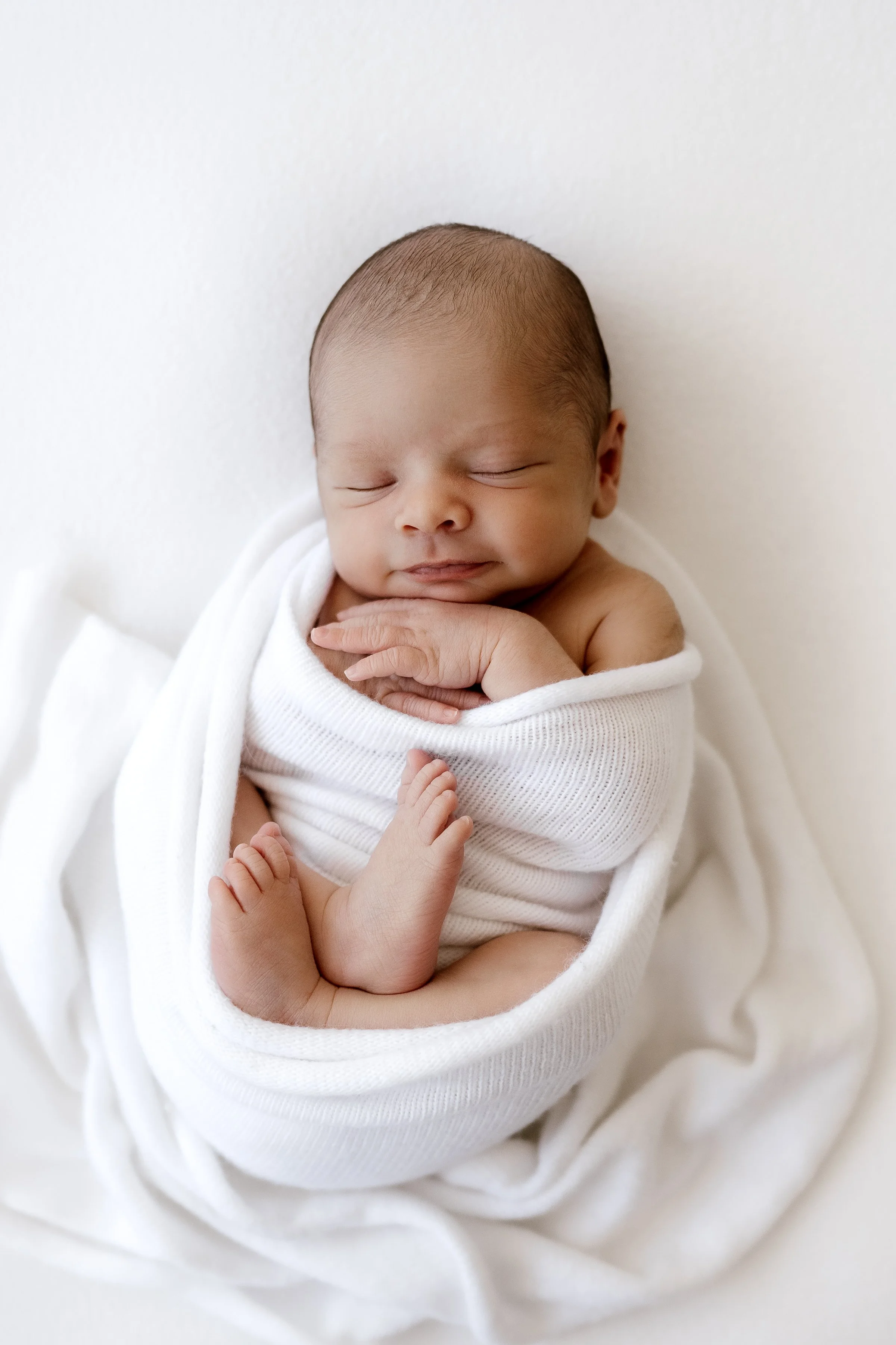 Close-up of a sleeping newborn baby wrapped in white blanket, resting peacefully.