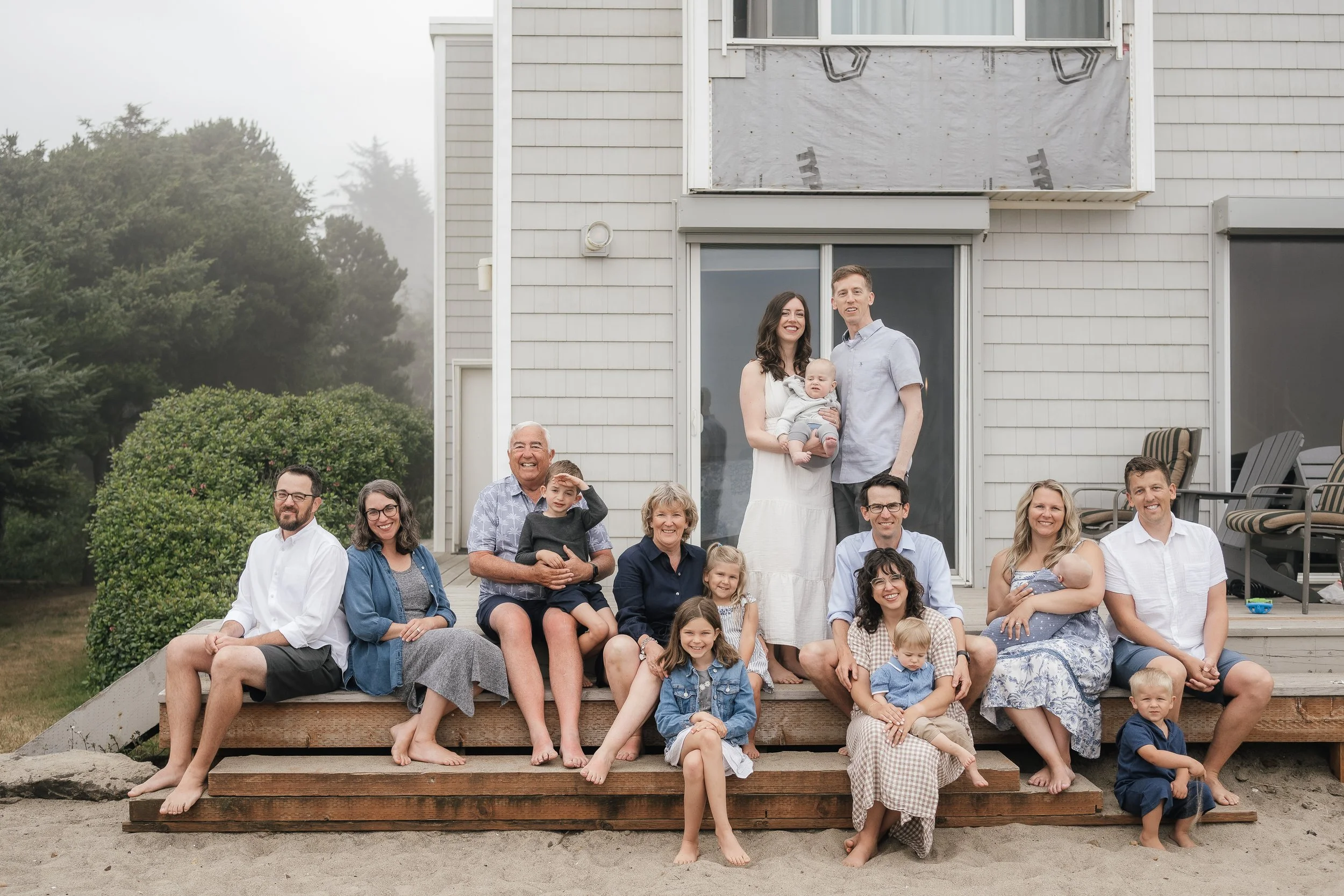 A large multigenerational family on a wooden deck in front of a house, smiling and posing for a photo, with several children and adults.