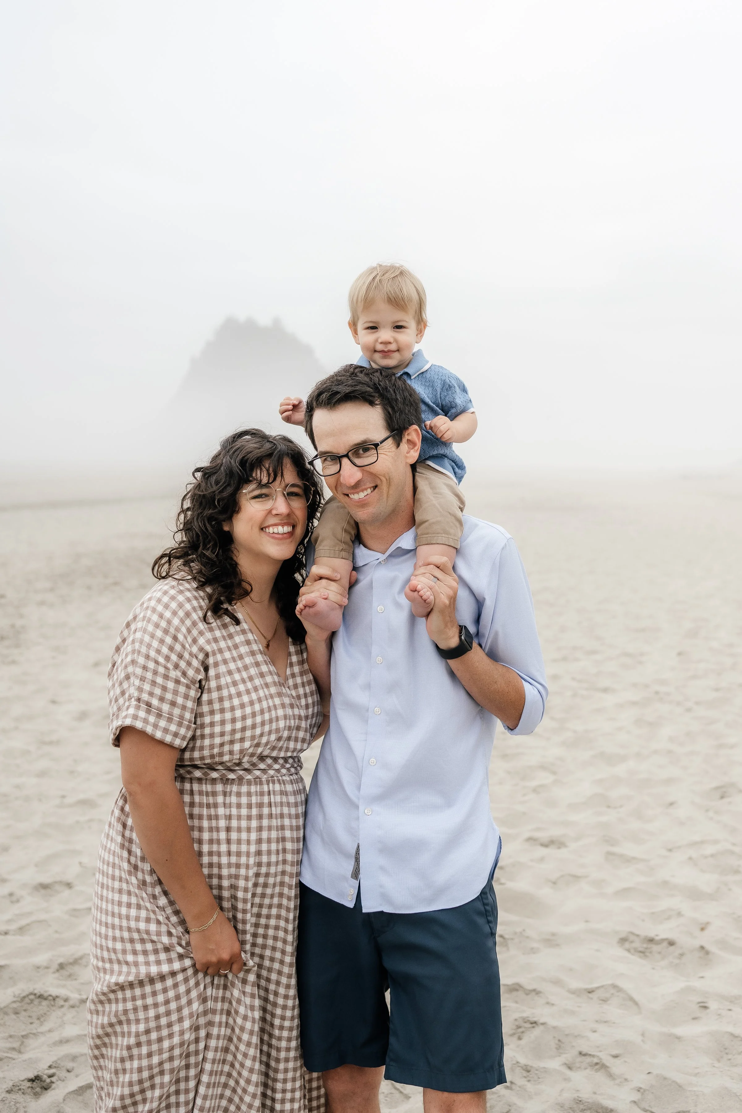 Family of three enjoying a day at the beach with a foggy background and a distant island