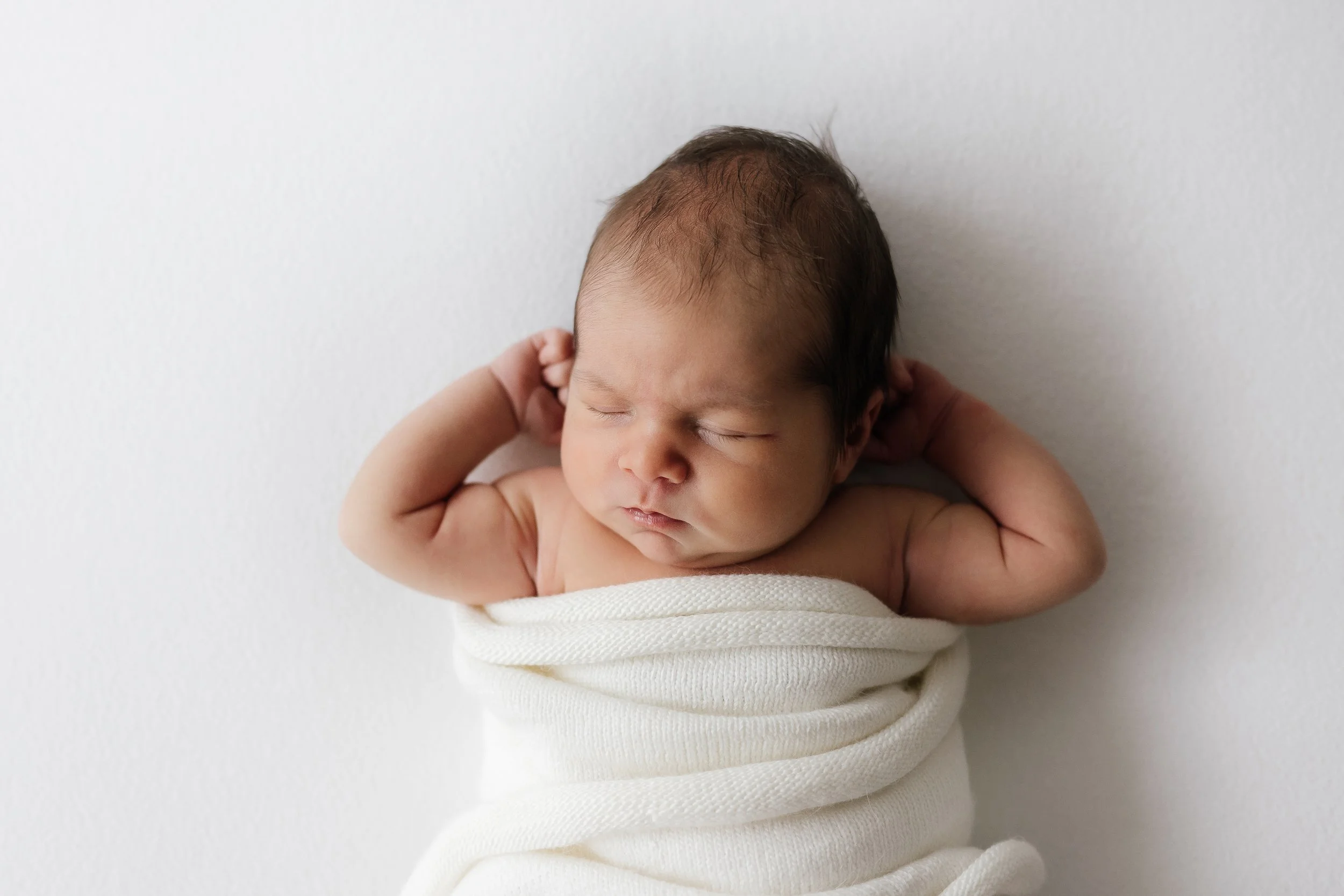 A sleeping newborn baby wrapped in a white blanket against a white background.