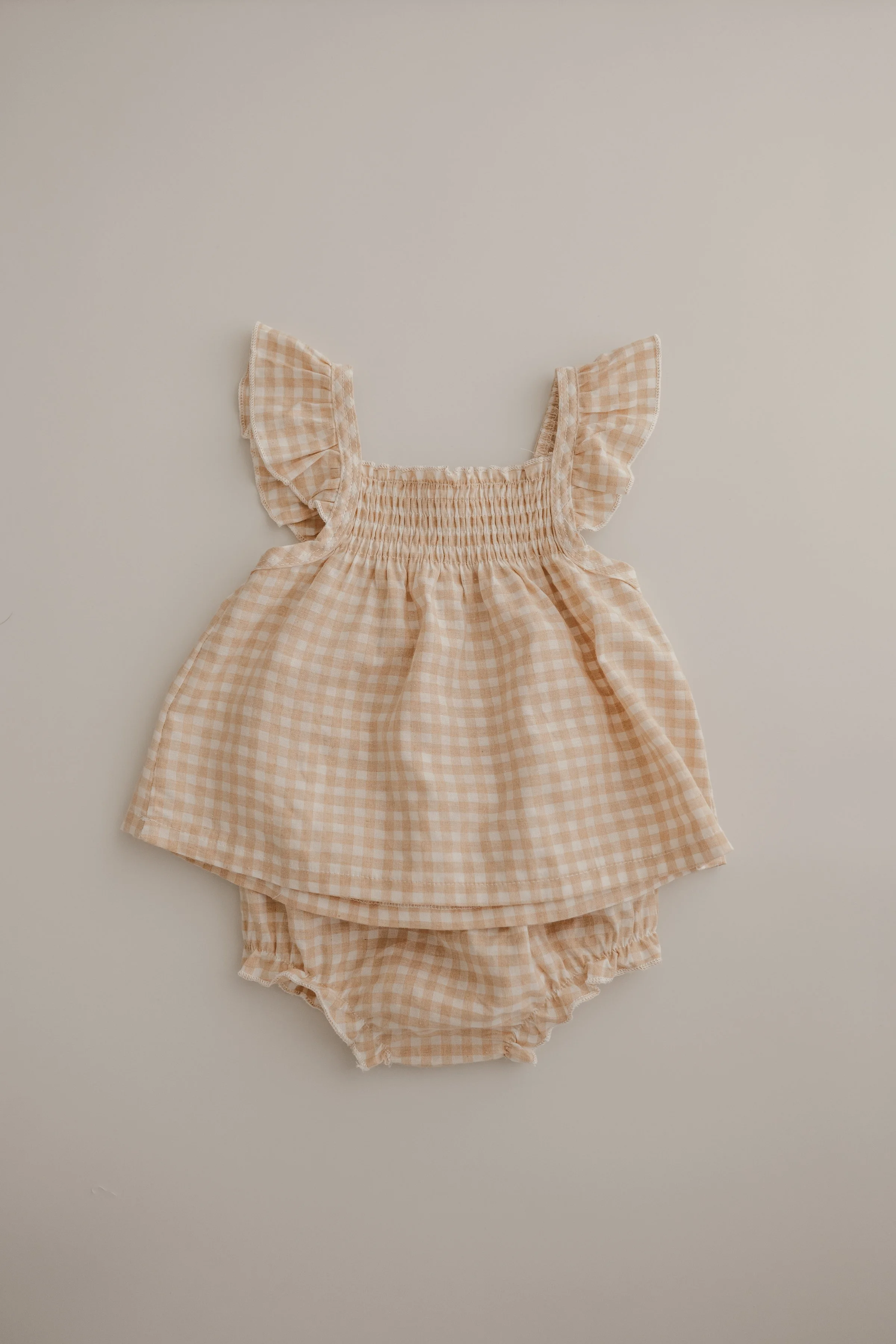 A peach-colored checkered baby dress with ruffled sleeves and matching checkered bloomers.