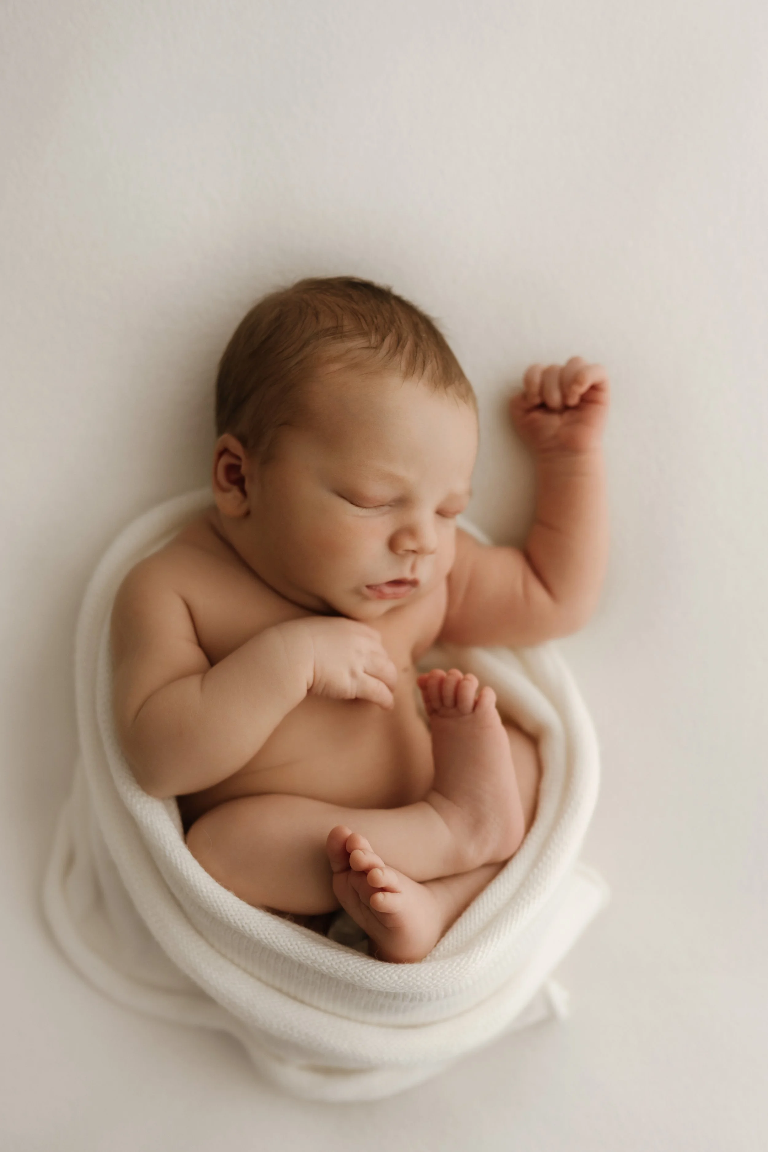 Newborn baby peacefully swaddled in white during a natural light studio session.