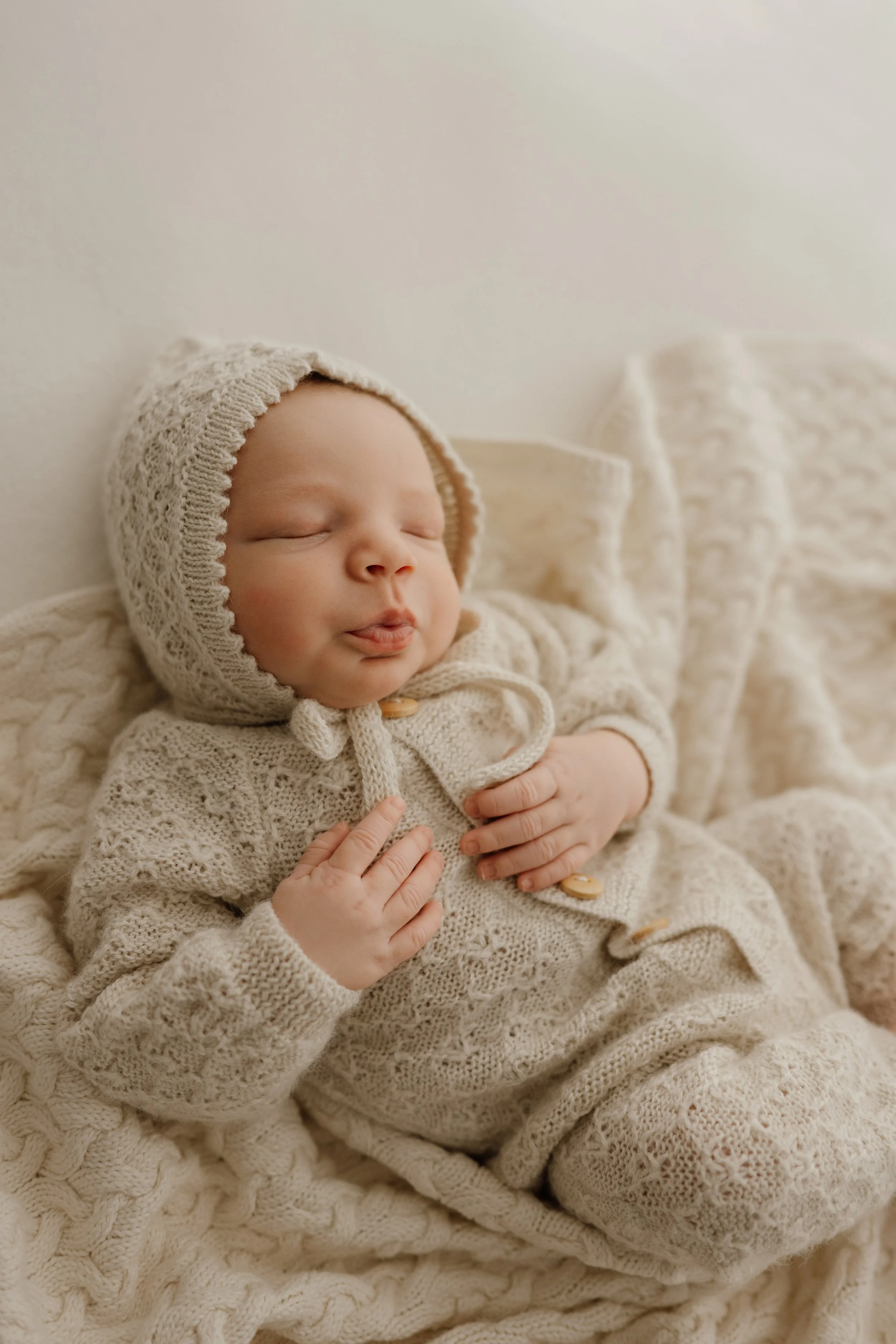 Newborn baby peacefully swaddled in white during a natural light studio session.