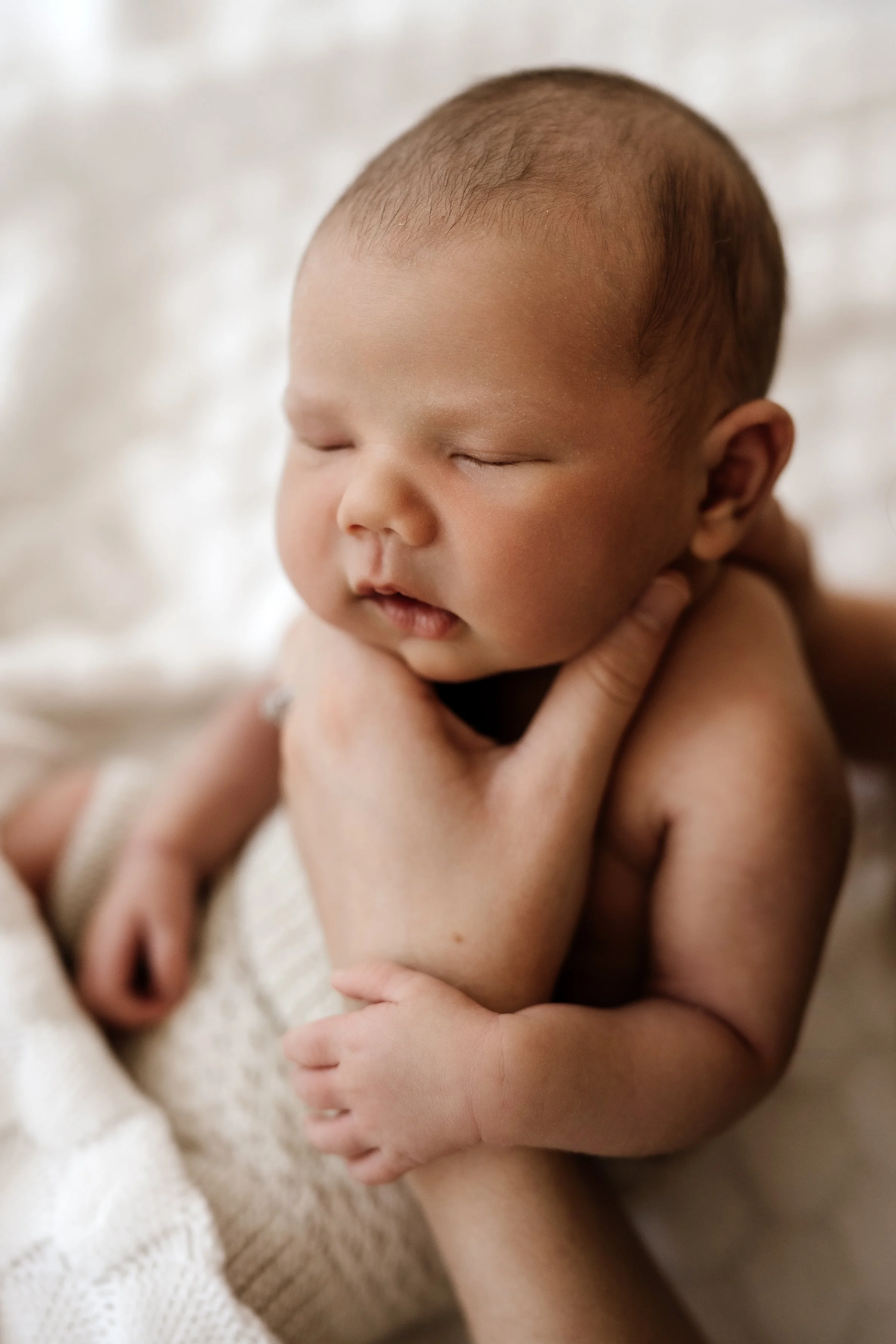 Close-up of a sleeping baby with a gentle hand supporting their neck and arm, wrapped in a soft blanket.