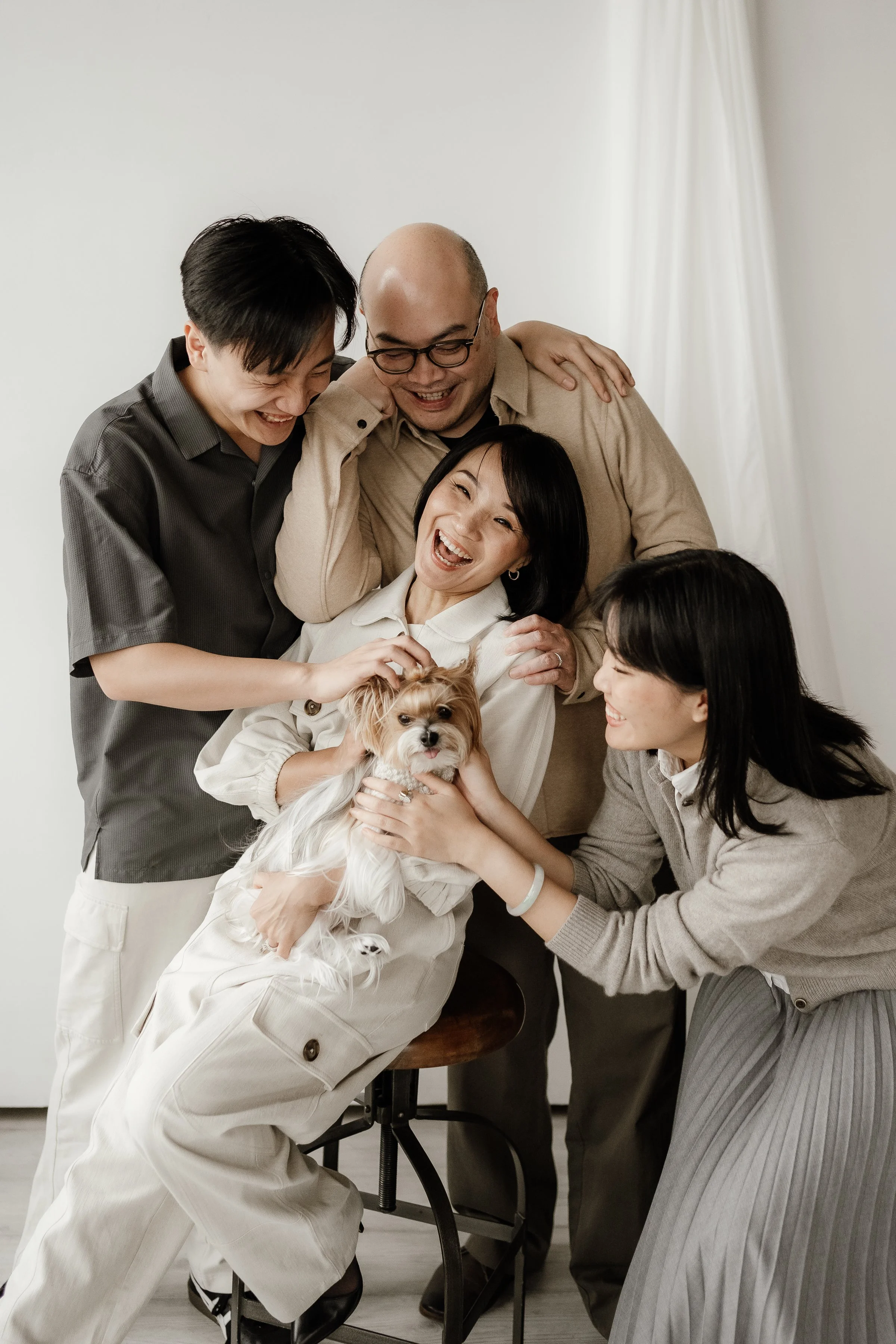 A group of five people and a dog in a joyful moment, some standing and some sitting, in front of a white background.