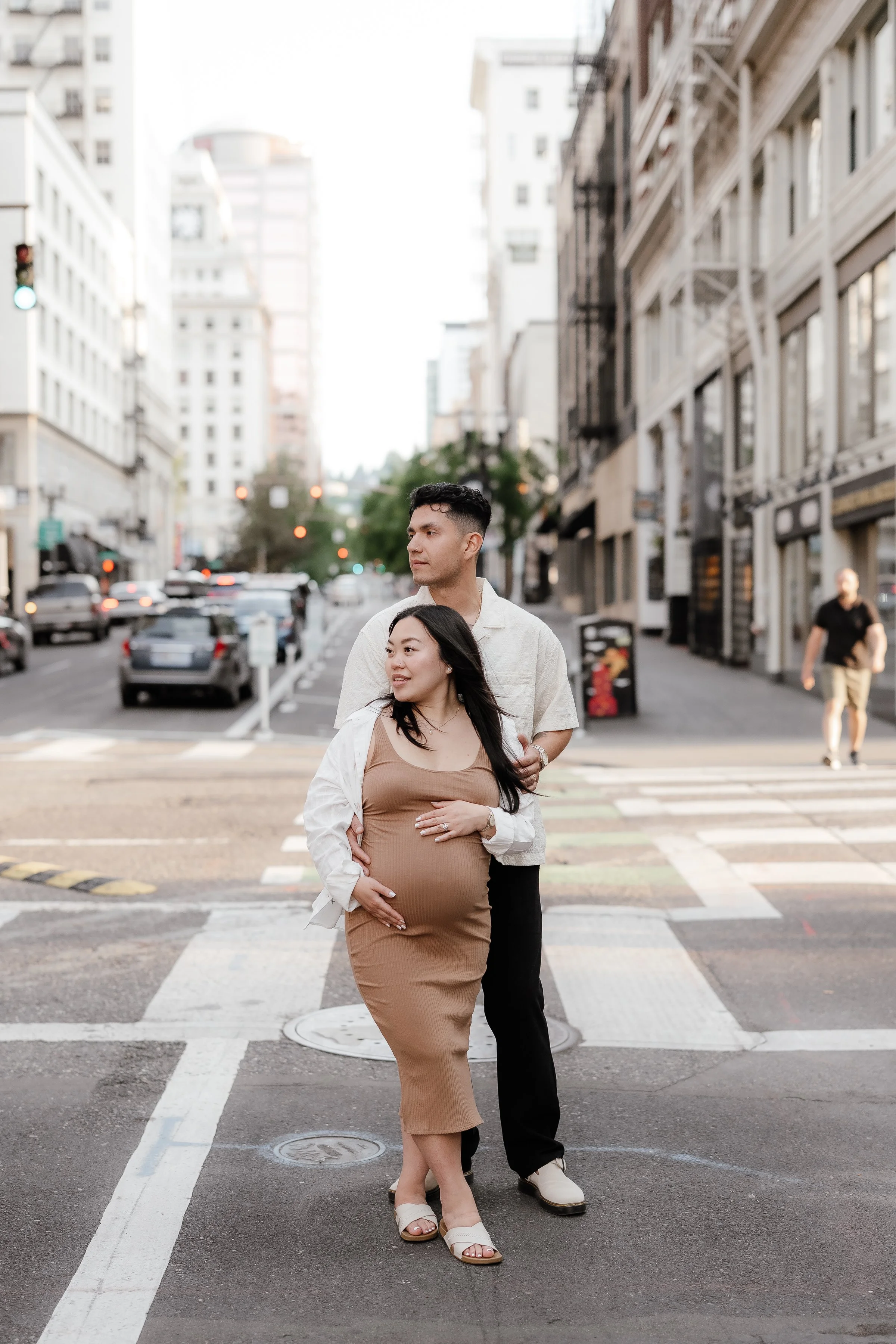 A pregnant woman and a man walking on a crosswalk in a city.