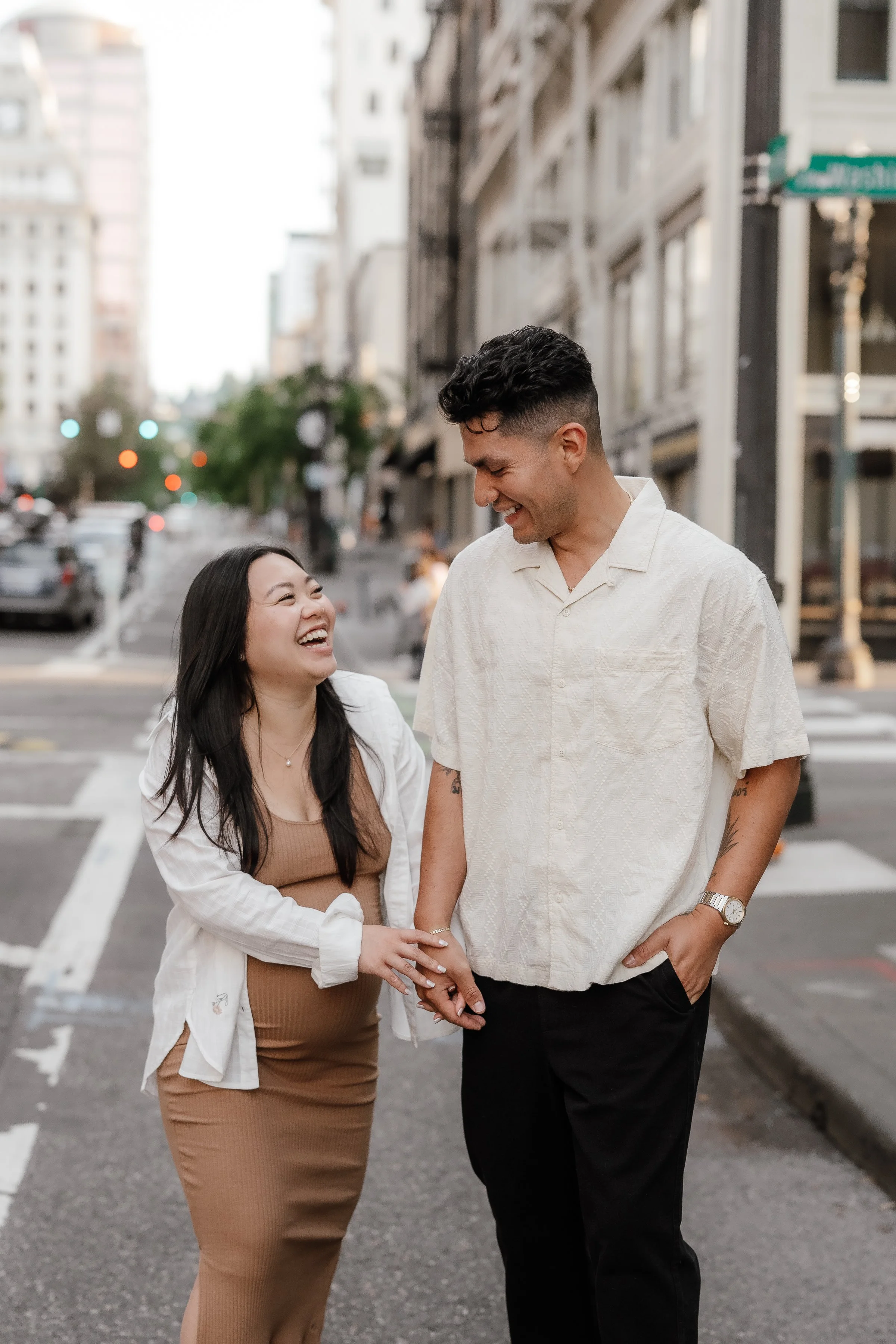 A happy couple holding hands and laughing on a city street during daytime.