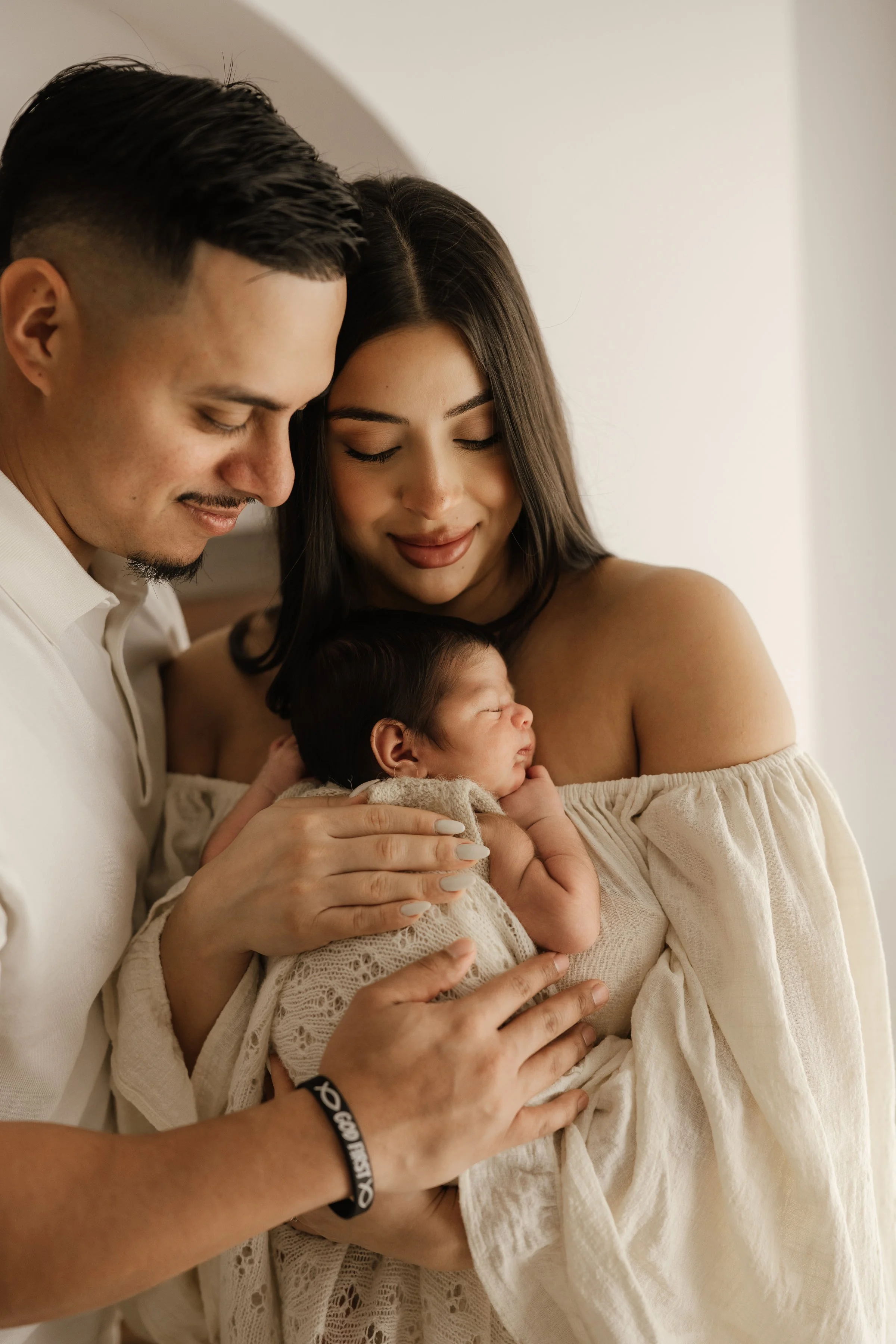 A couple holding their newborn baby, smiling and looking lovingly at the baby.