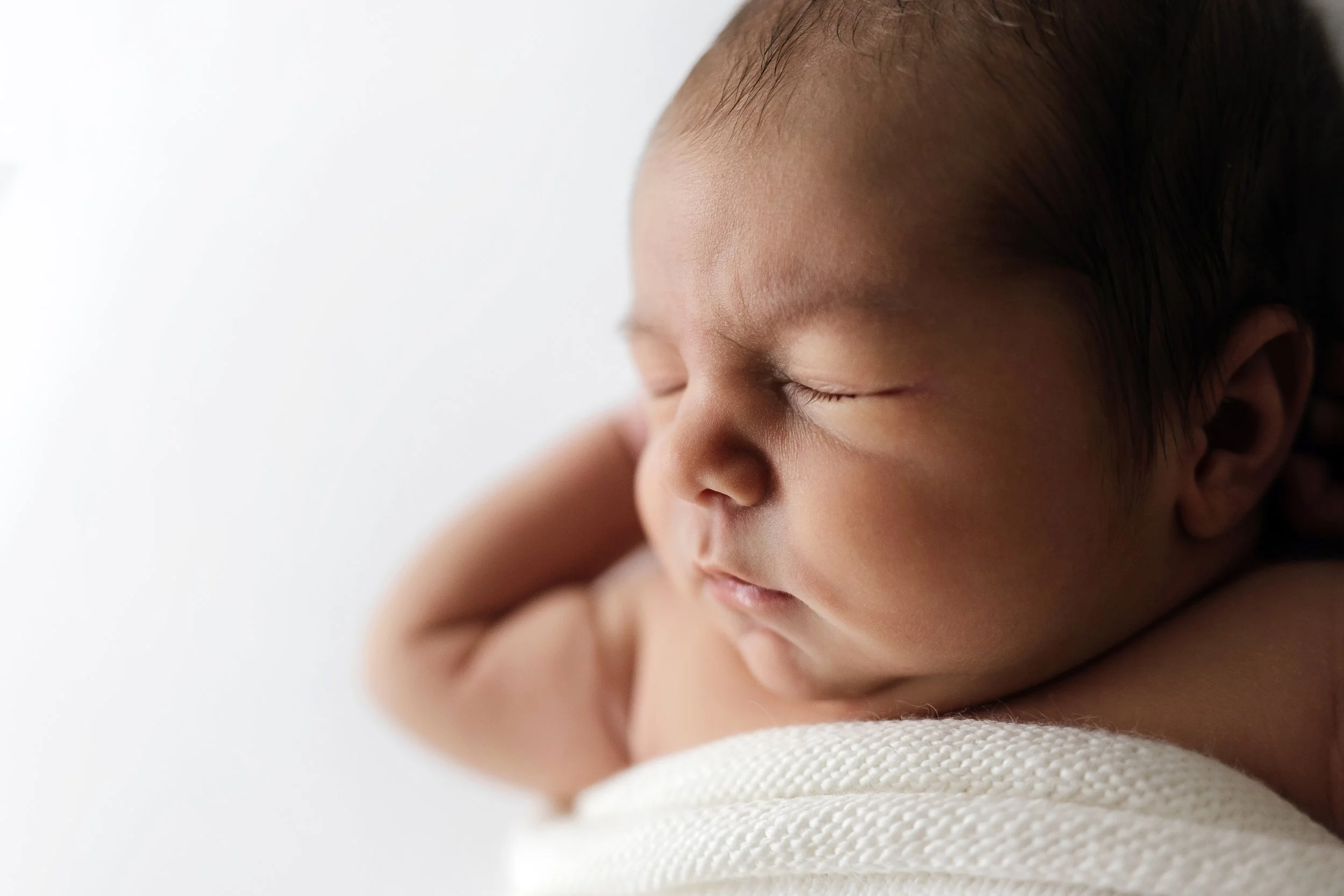 Close-up of a sleeping baby with closed eyes, resting on a soft white surface.