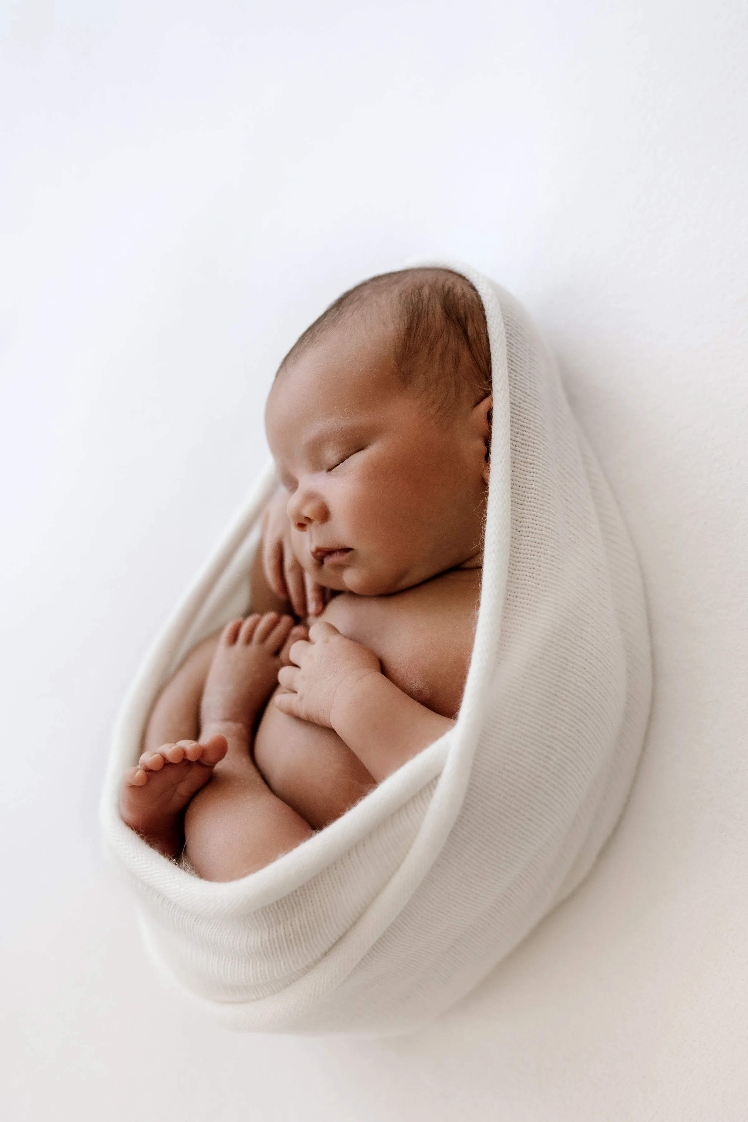 A sleeping newborn baby wrapped in a white blanket.