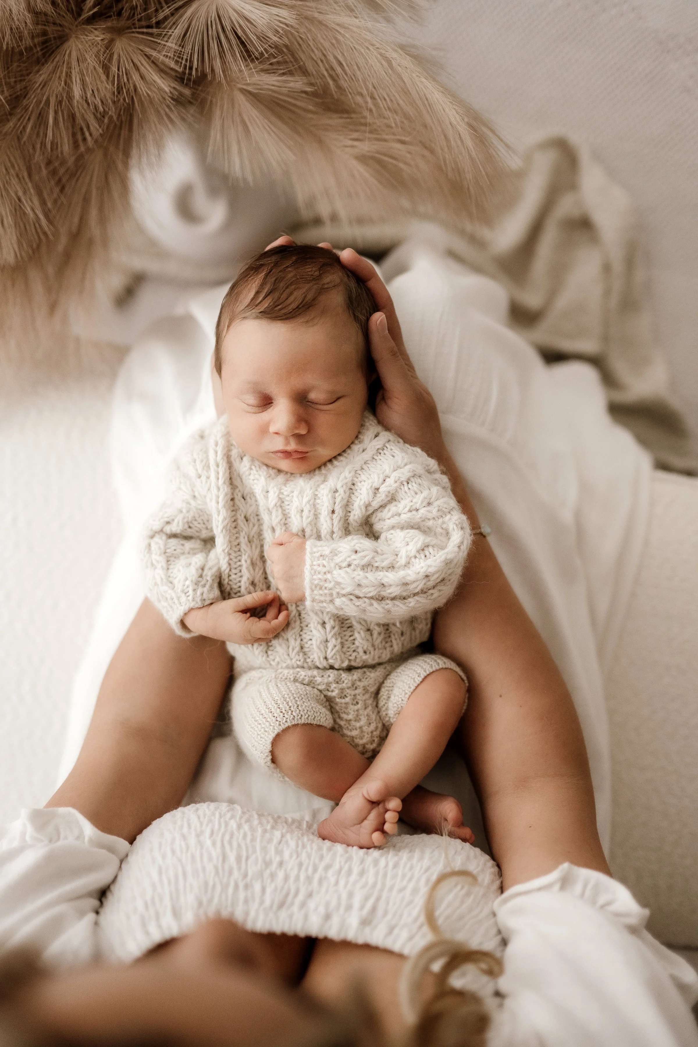 Close-up of a newborn baby sleeping on a person's lap, dressed in a cozy knit sweater and shorts.