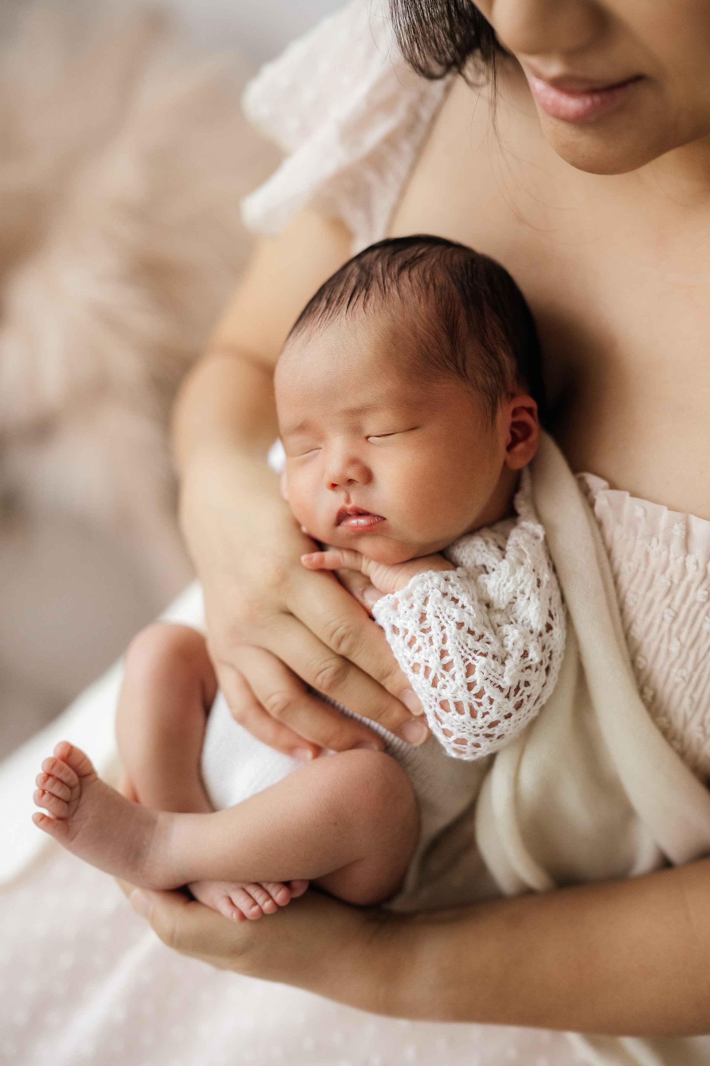 A woman cradling a sleeping baby with closed eyes and relaxed expression, in a cozy indoor setting.