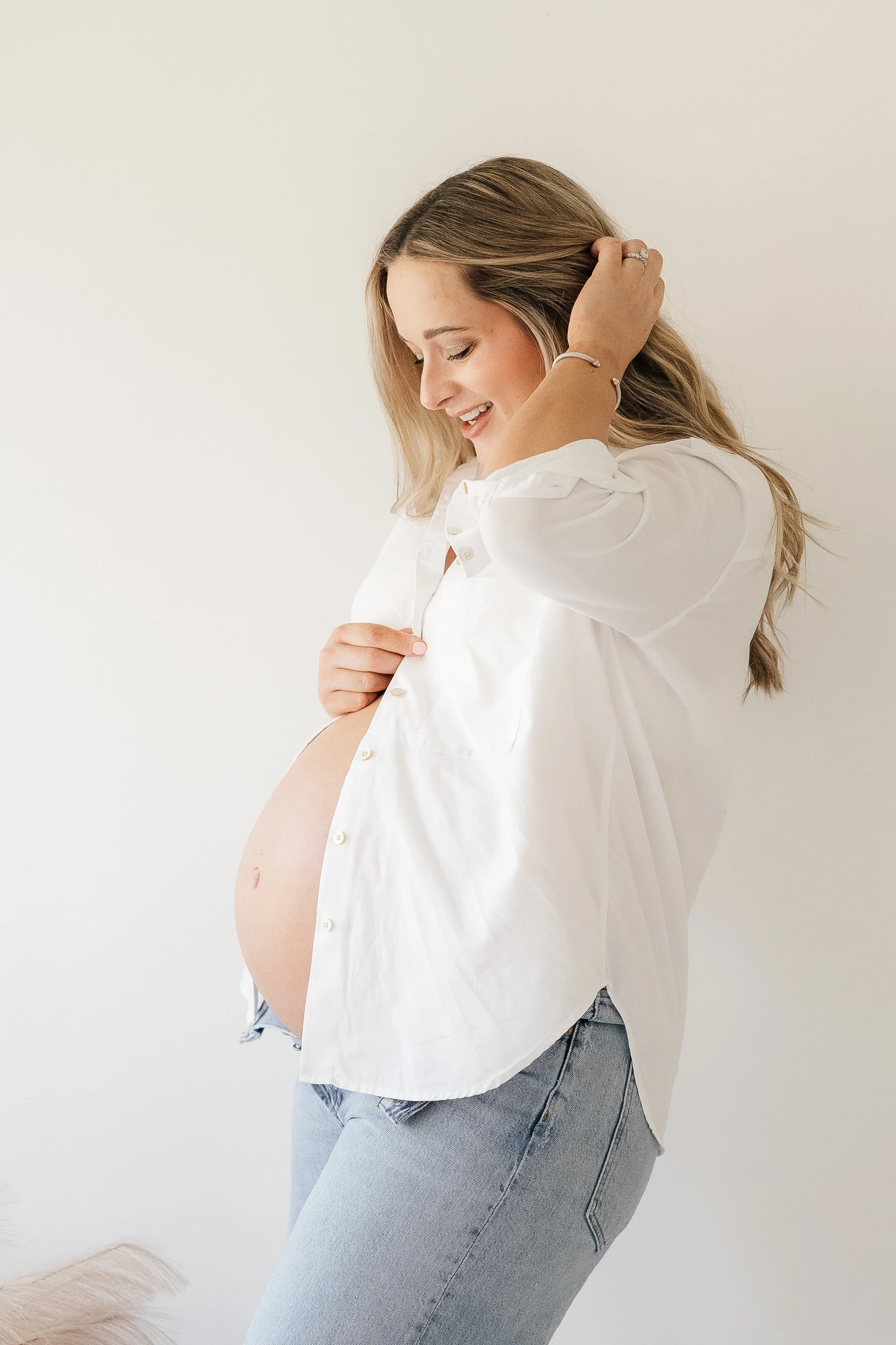 Pregnant woman smiling while holding her belly and touching her hair.