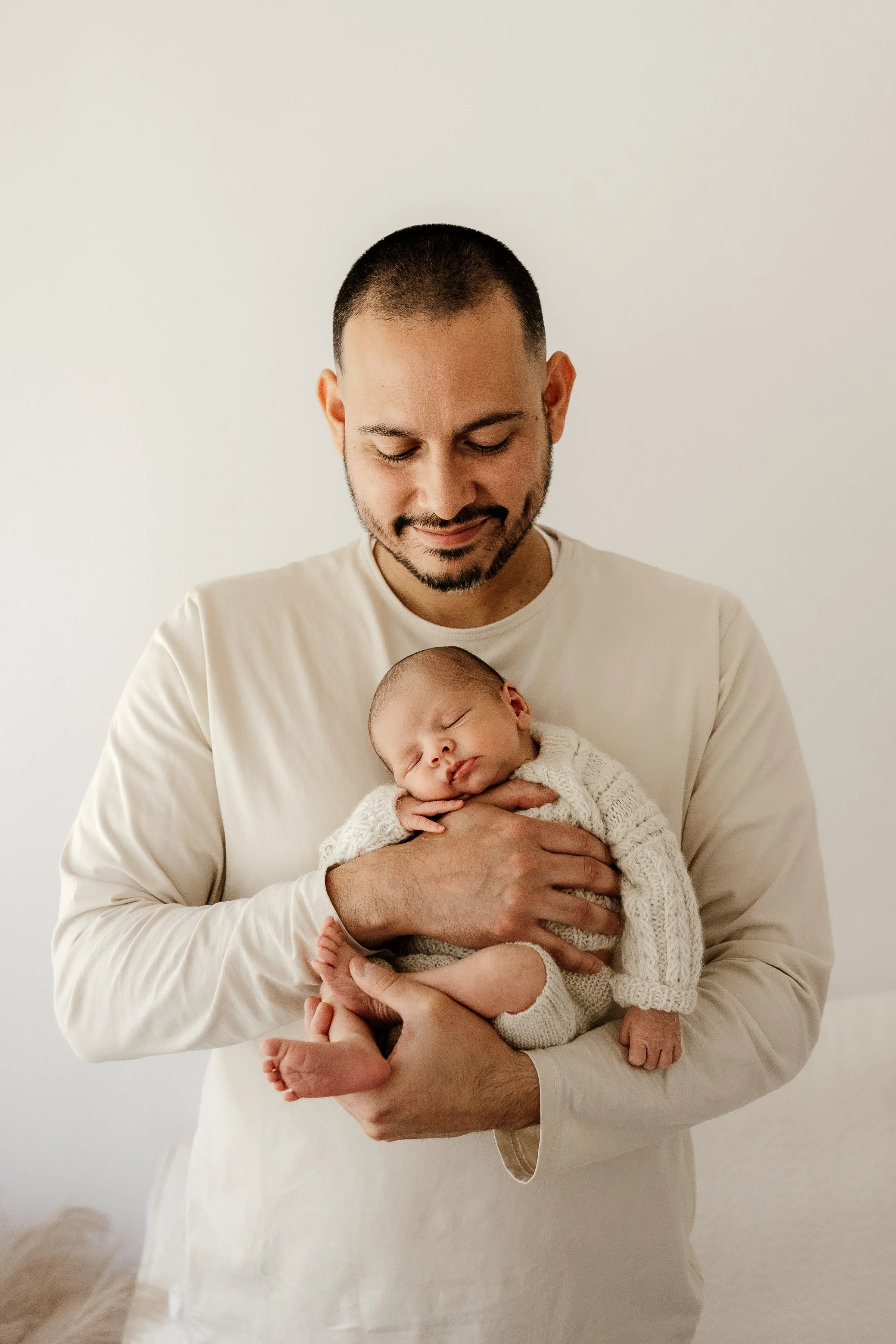 A man holding a sleeping newborn baby in his arms.