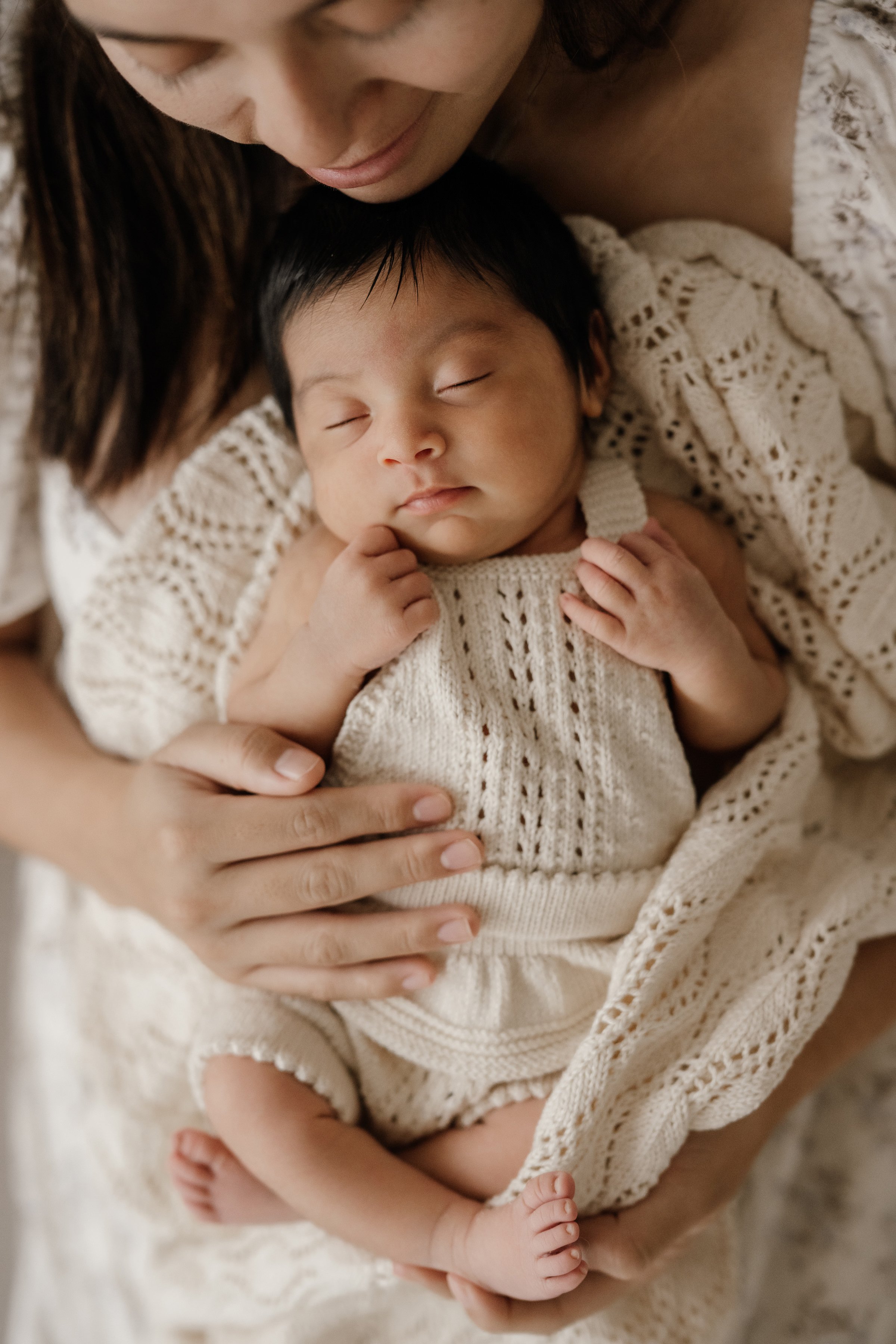A woman holding a sleeping baby dressed in cream-colored knitted clothing.