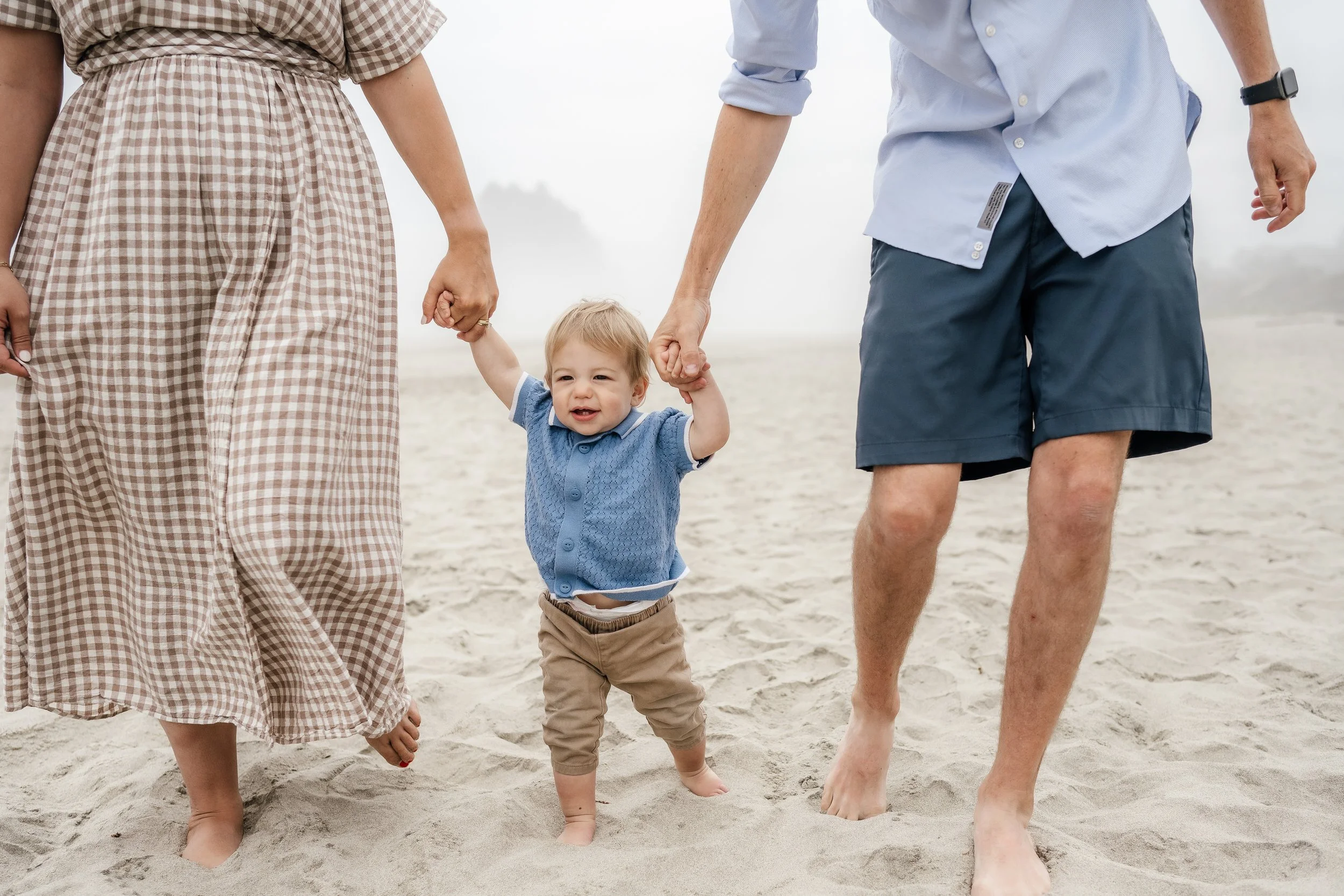 Young boy being supported by parents while walking on the beach.