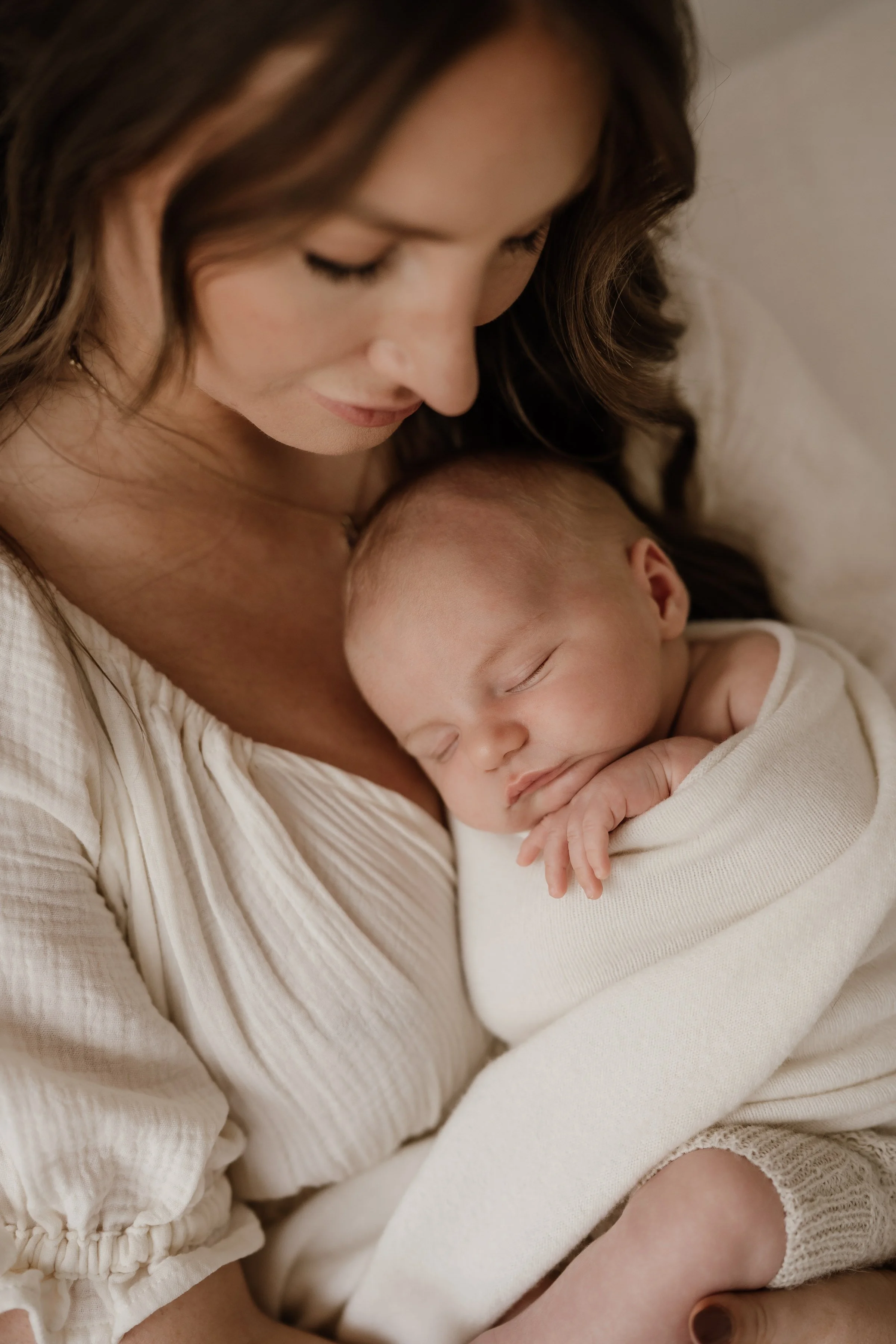 A woman holding a sleeping baby close to her chest, both with peaceful expressions, in soft lighting.